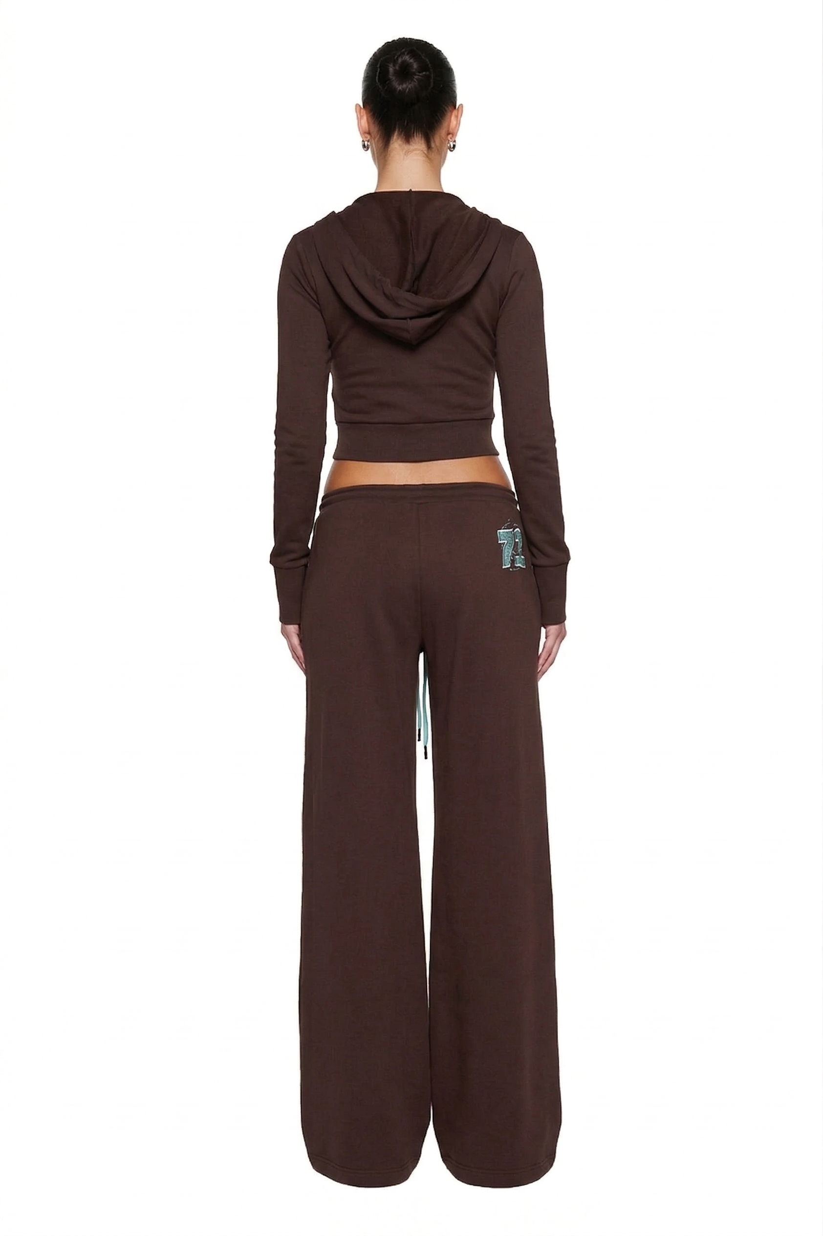 A woman, back to camera, wears a chocolate brown french terry hooded crop top and I.AM.GIA ARLO TRACK PANT - BROWN AND BLUE with patch on the back pocket, posing against a white background.
