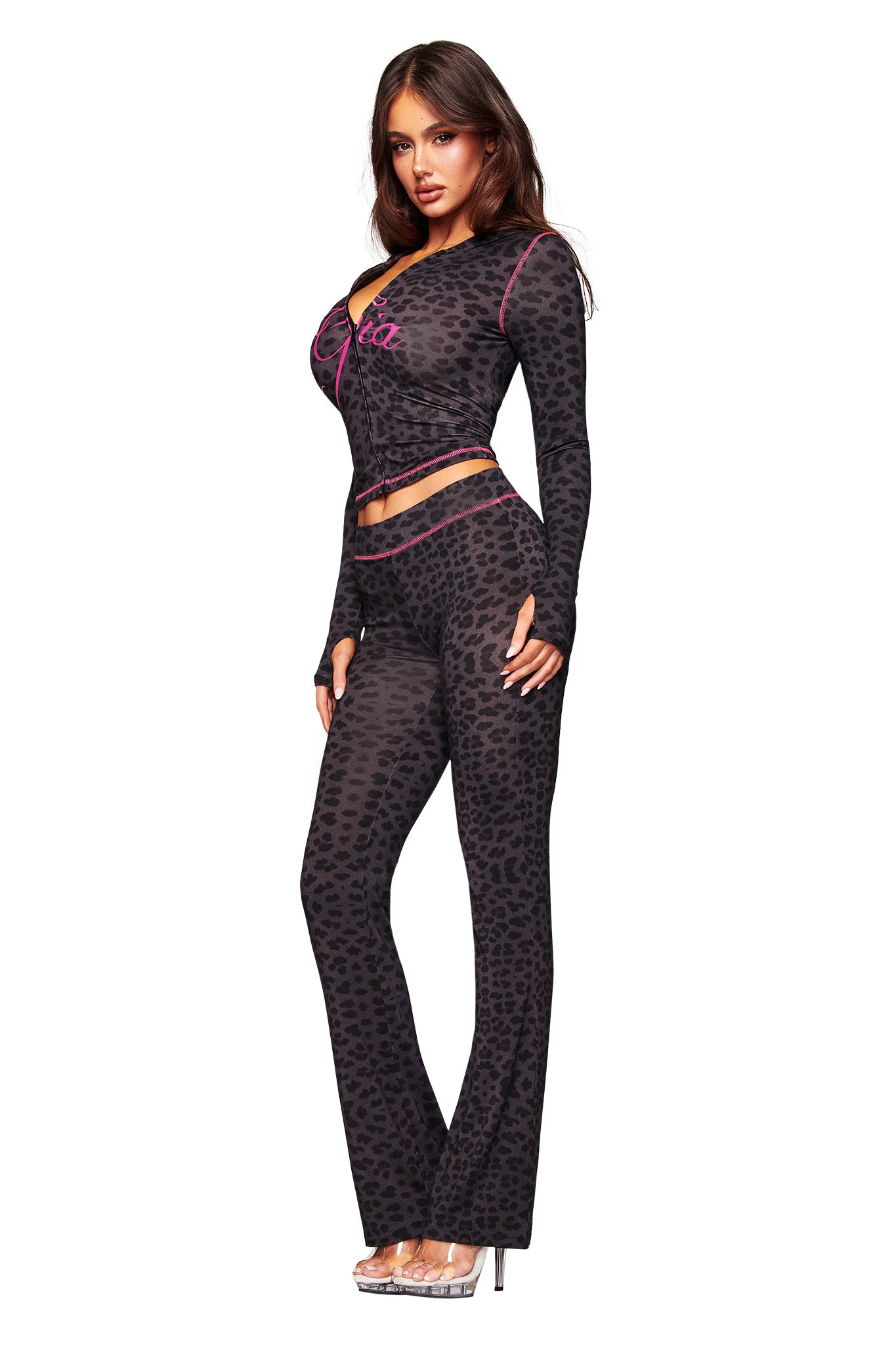 A woman wears the I.AM.GIA BLARE TRACKPANT in panther print with a matching fitted top, styled with clear high heels, posing against a white background.