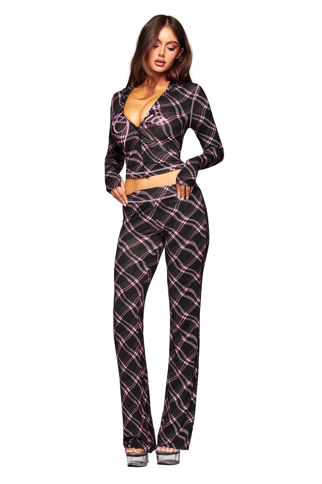 A woman poses in I.AM.GIA's BLARE TRACKPANT - BLACK WARPED PLAID, styled with a matching deep V-neck crop top and silver platform heels, set against a white background.