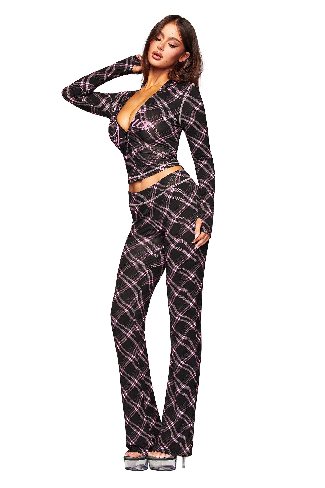 A woman poses in I.AM.GIA’s BLARE TRACKPANT - BLACK WARPED PLAID, styled with a matching long-sleeve crop top in black, pink, and white plaid, and silver platform heels.