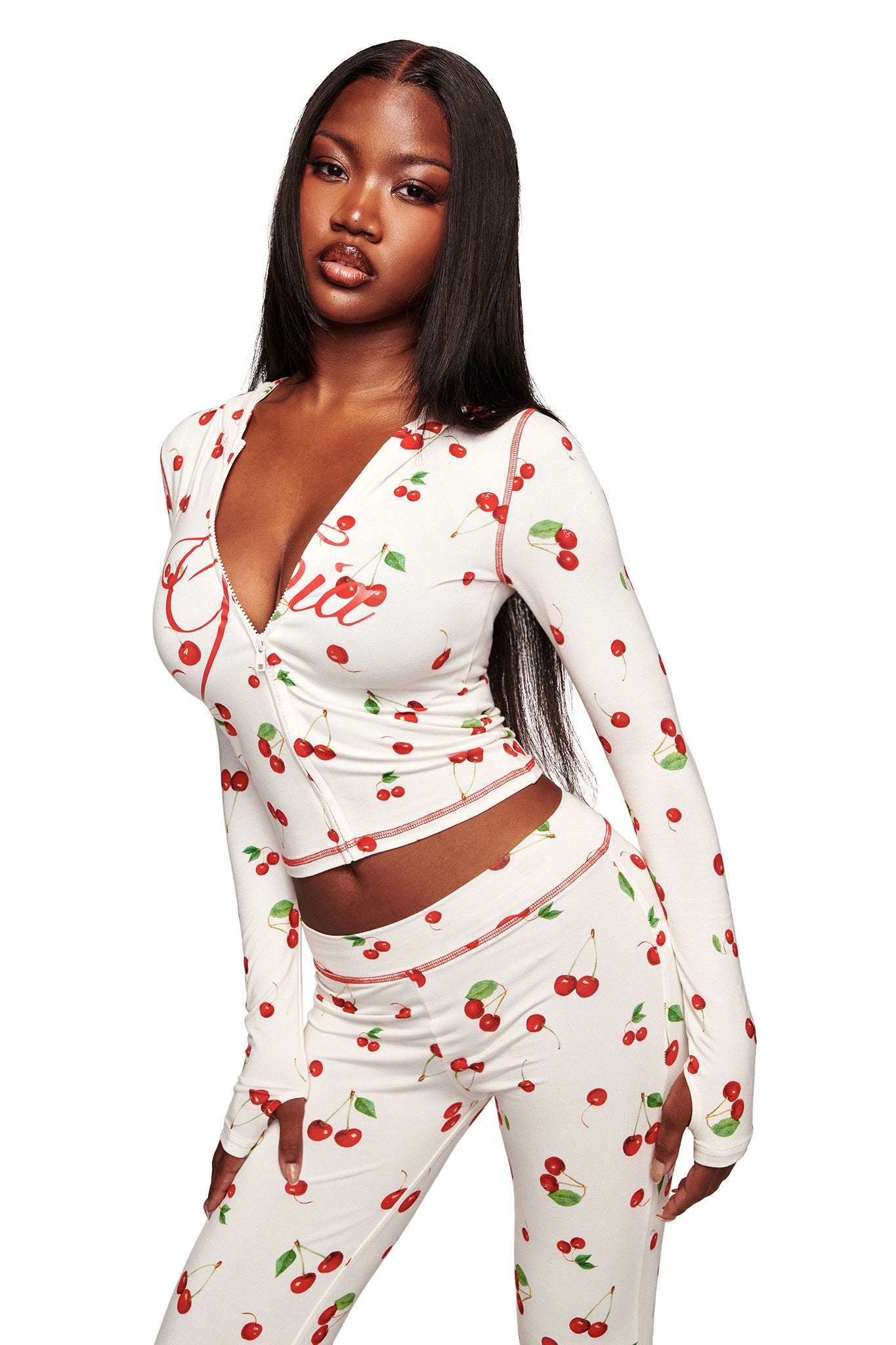 A woman models the I.AM.GIA BLARE TRACKPANT - CHERRY ON TOP, a fitted white trackpant with red cherry and green leaf prints, paired with a matching deep V-neck top featuring "Juice" on the chest for a vibrant, bold look.