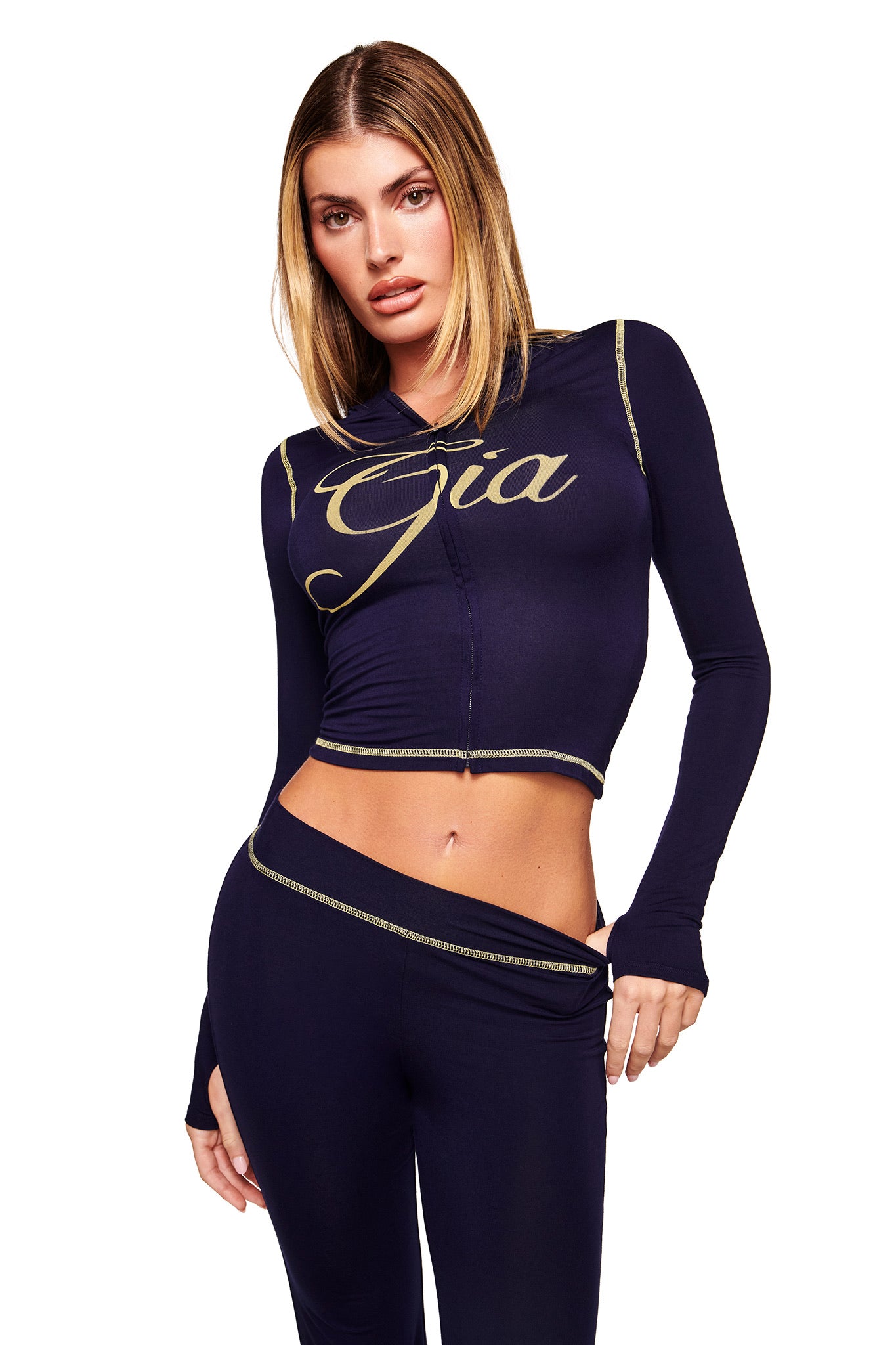 A woman in the I.AM.GIA "BLARE HOODIE - NAVY" poses confidently against a white background, showcasing her straight blonde hair and self-assured expression.