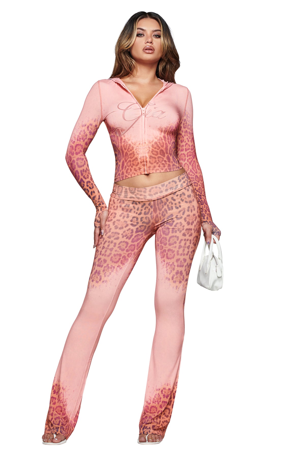 A woman wearing the I.AM.GIA BLARE HOODIE in Pink Faded Panthera print with matching flared pants, holding a small white handbag, stands against a white background.