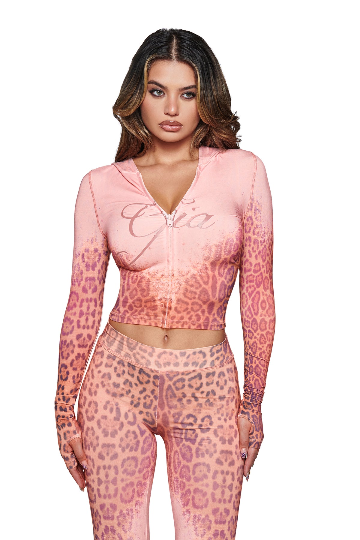 A woman wearing the I.AM.GIA BLARE HOODIE in Pink Faded Panthera—a zip-up cropped style—paired with matching high-waisted leggings, both made from soft bamboo fabric, stands against a white background.