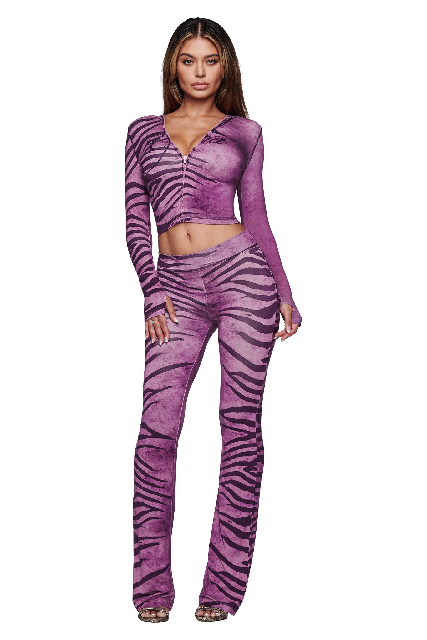 A woman with long brown hair wears the I.AM.GIA BLARE HOODIE in Plum Wild Side, paired with matching flare pants and high-heeled sandals, standing against a white background.