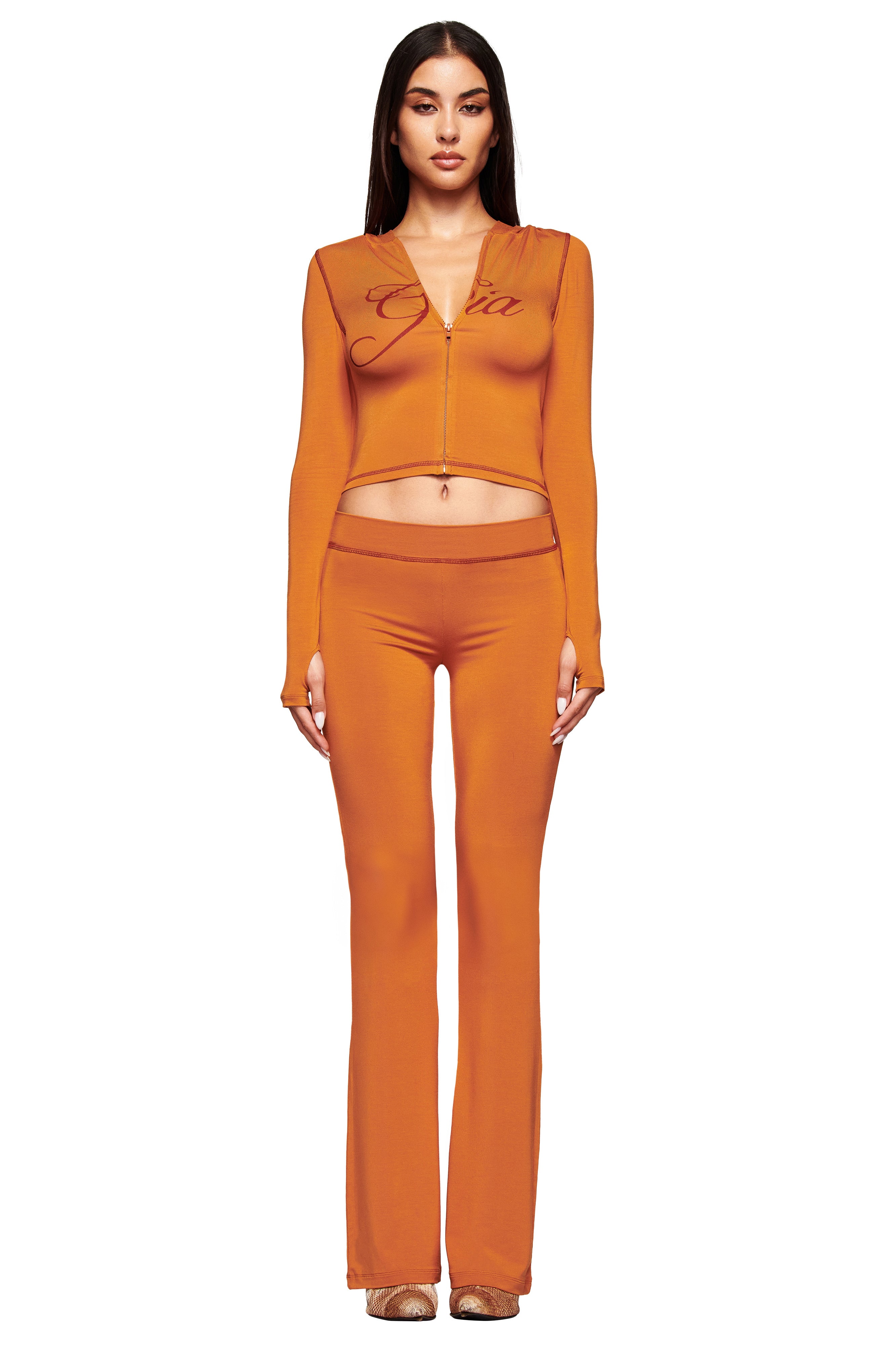A woman wears I.AM.GIA's BLARE TRACKPANT in Pumpkin, styled with a low-rise waist and an orange outfit.