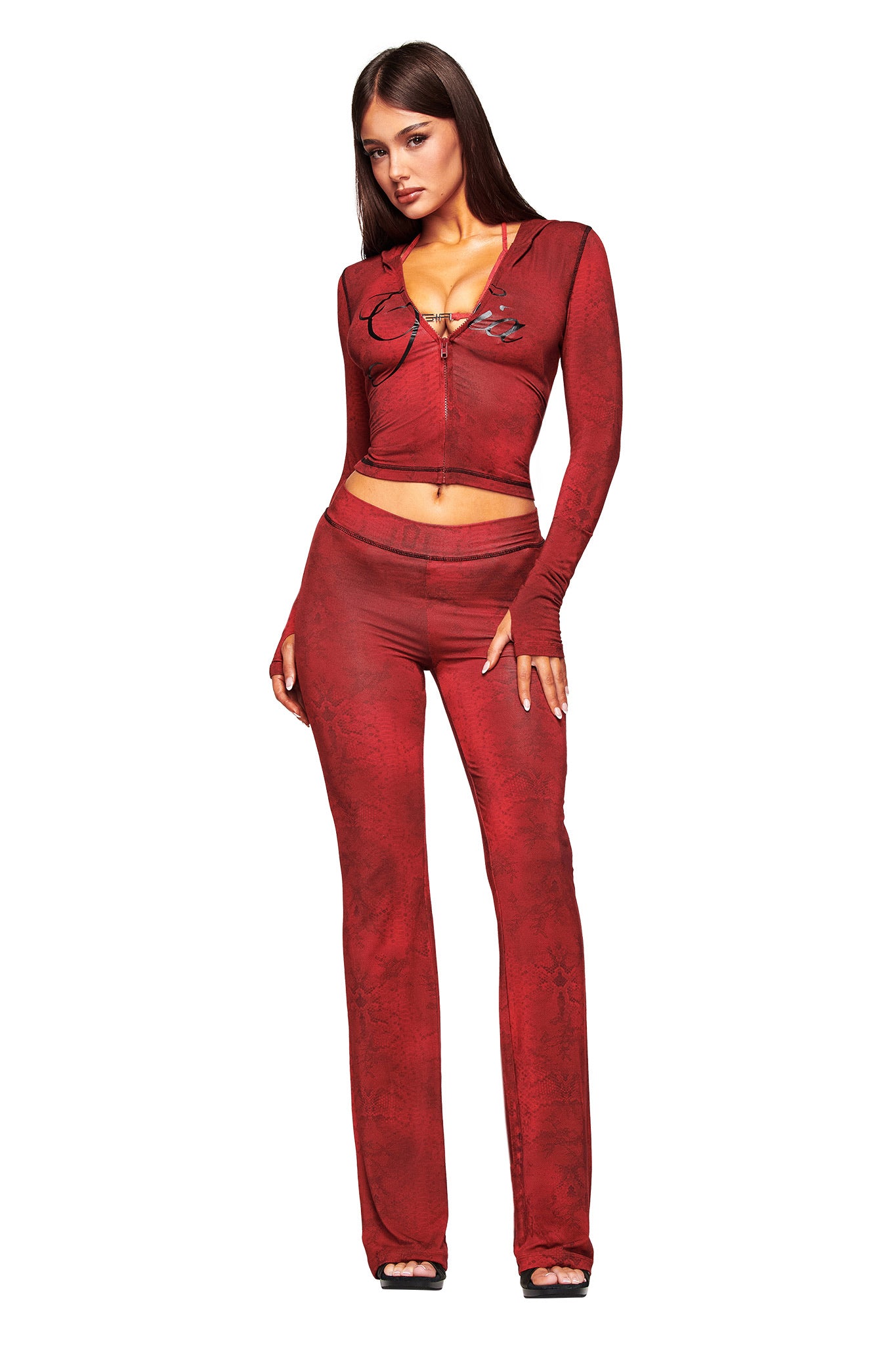 A woman wears the I.AM.GIA BLARE HOODIE in red serpentine, a fitted, long-sleeve crop top with tie-front detail and matching high-waisted flared pants, styled with open-toe heels against a white background.