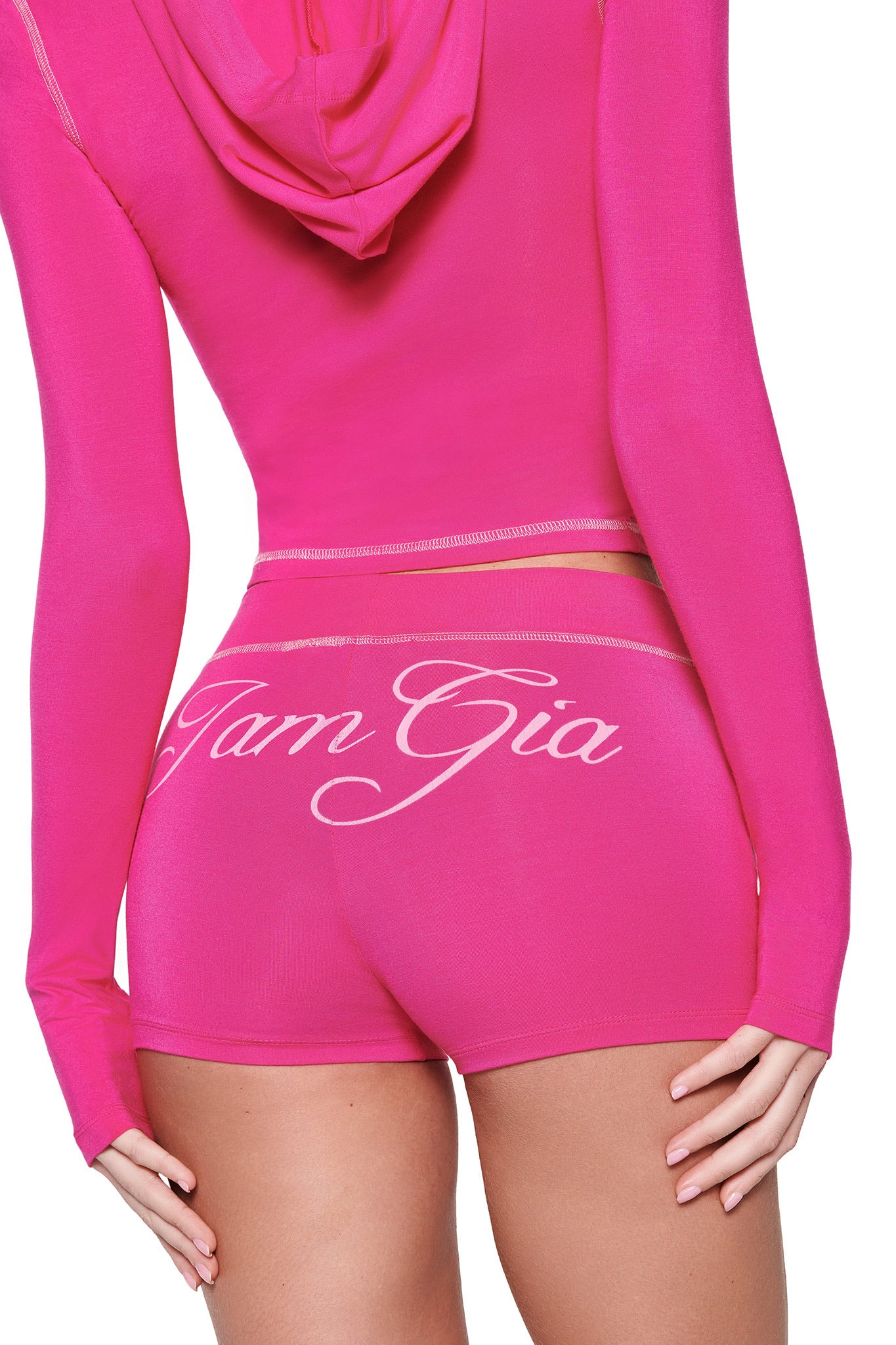 A person in a hot pink I.AM.GIA hoodie and BLARE SHORT, made from stretchy bamboo fabric, stands with their back to the camera. The outfit hugs their form and showcases the vivid color brilliantly.