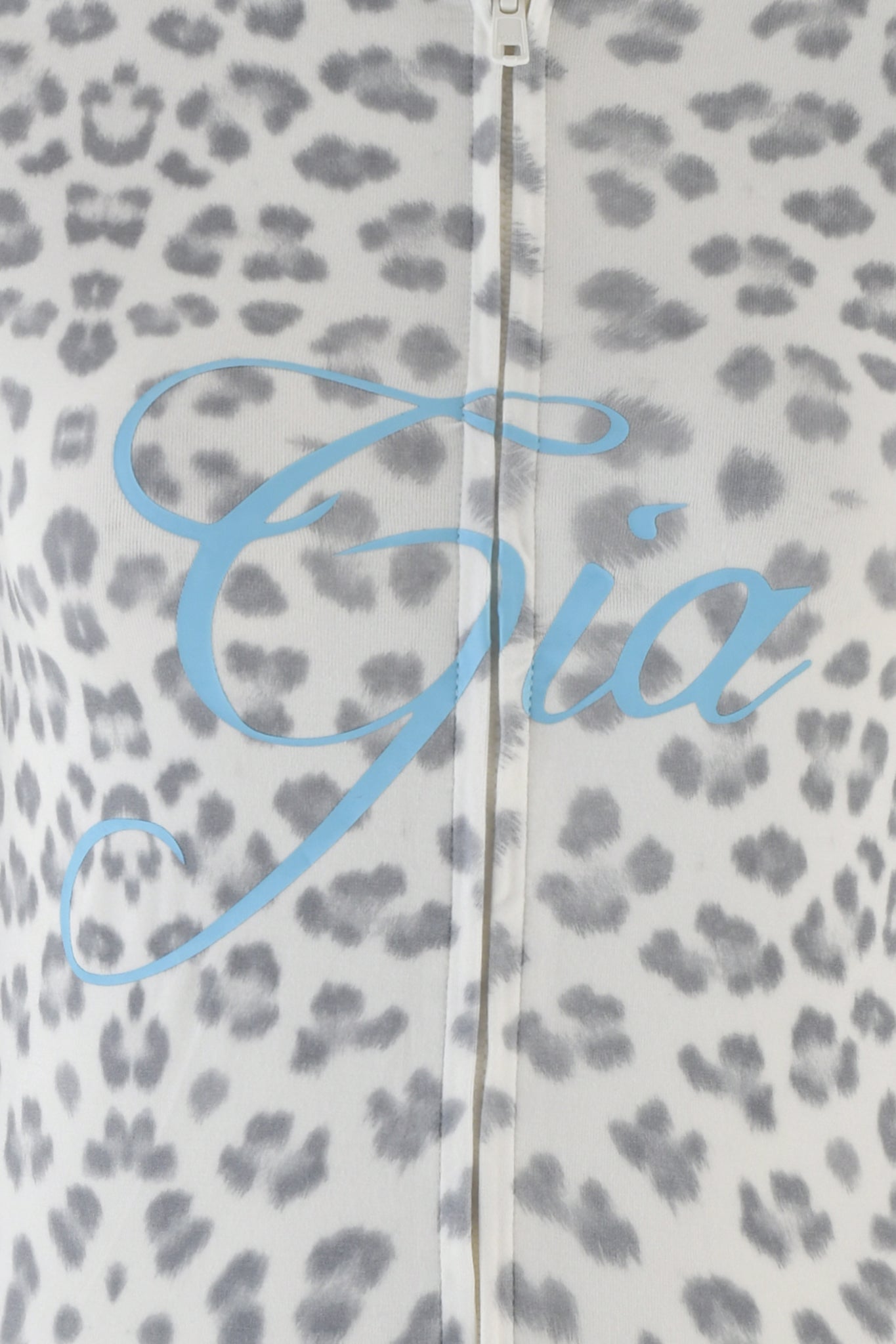 A close-up of the BLARE HOODIE - SNOW LEOPARD: WINTER WILD CARD by I.AM.GIA showcases a snow leopard print fabric with gray spots on a white background. The brand name "I.AM.GIA" is elegantly scripted in blue cursive across the middle, adding a touch of chic style. A zipper runs vertically through the center, hinting at the sleek bodycon fit of this design.