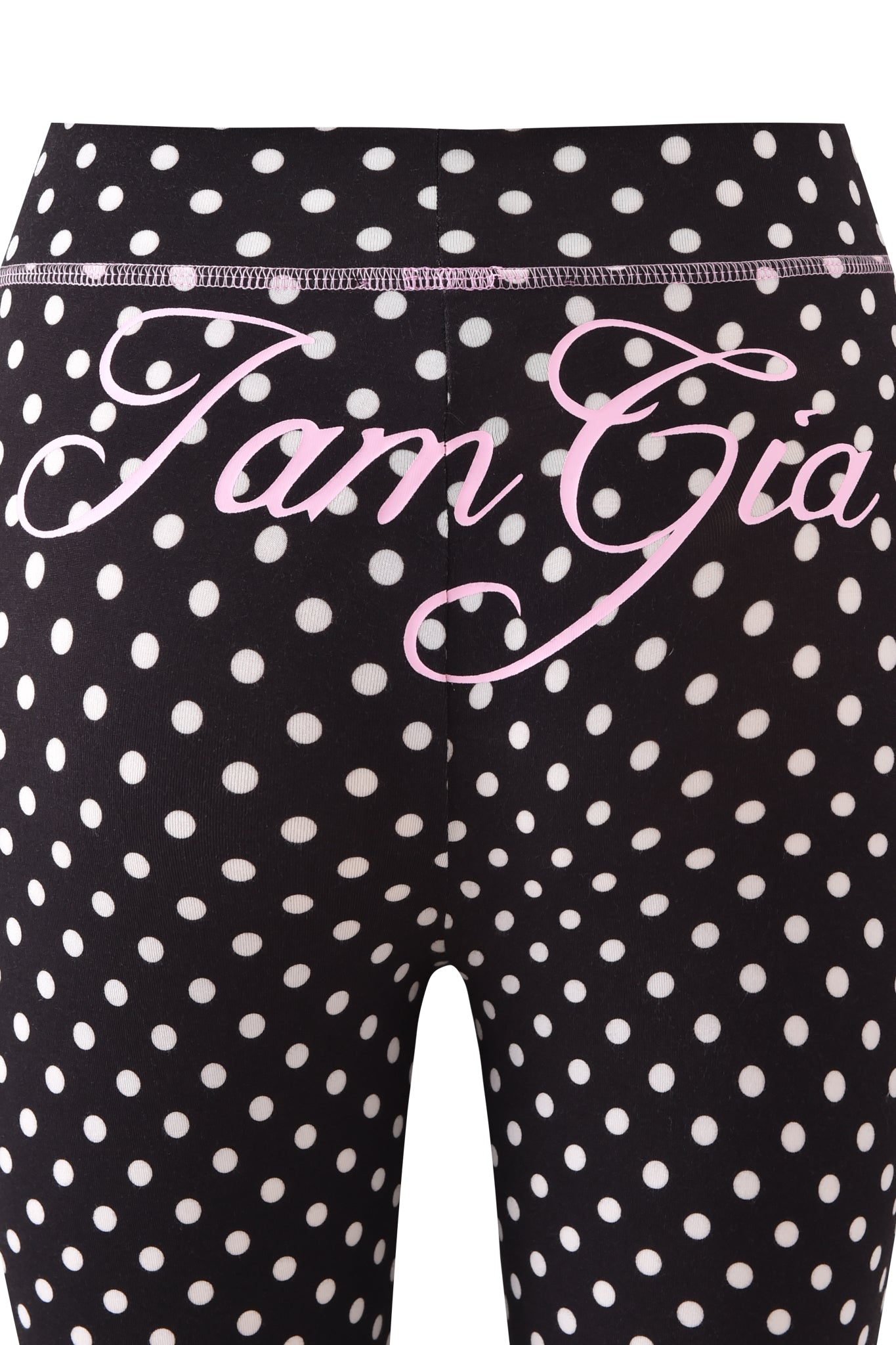 Close-up of BLARE TRACKPANT - BLACK POLKA DOT by I.AM.GIA, featuring playful polka dots and "I.AM.GIA" in pink cursive across the waistband and upper hips.