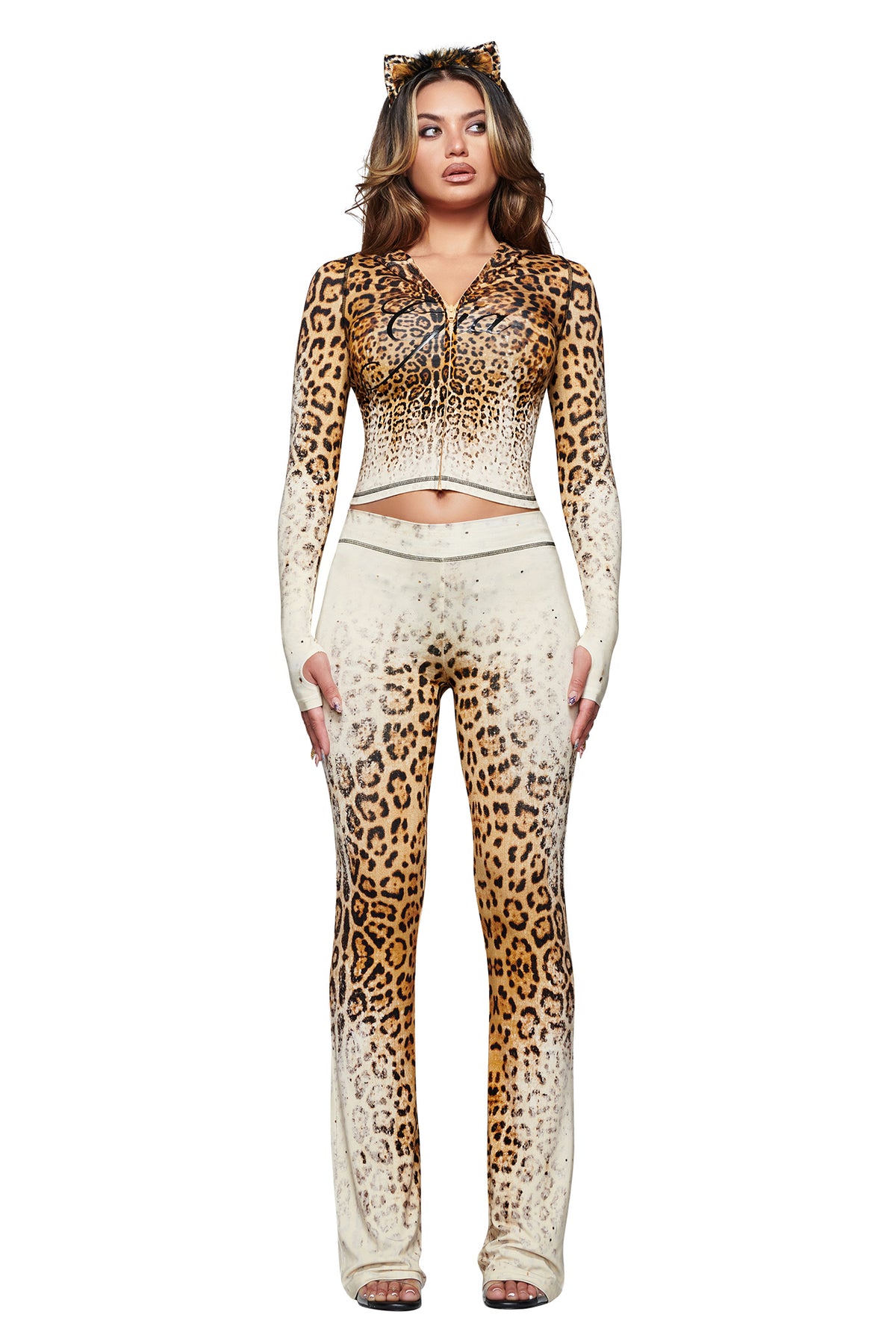 A woman wearing the I.AM.GIA BLARE TRACKPANT in Cream Faded Panthera with a matching zip-up top and cat ears stands against a white background.