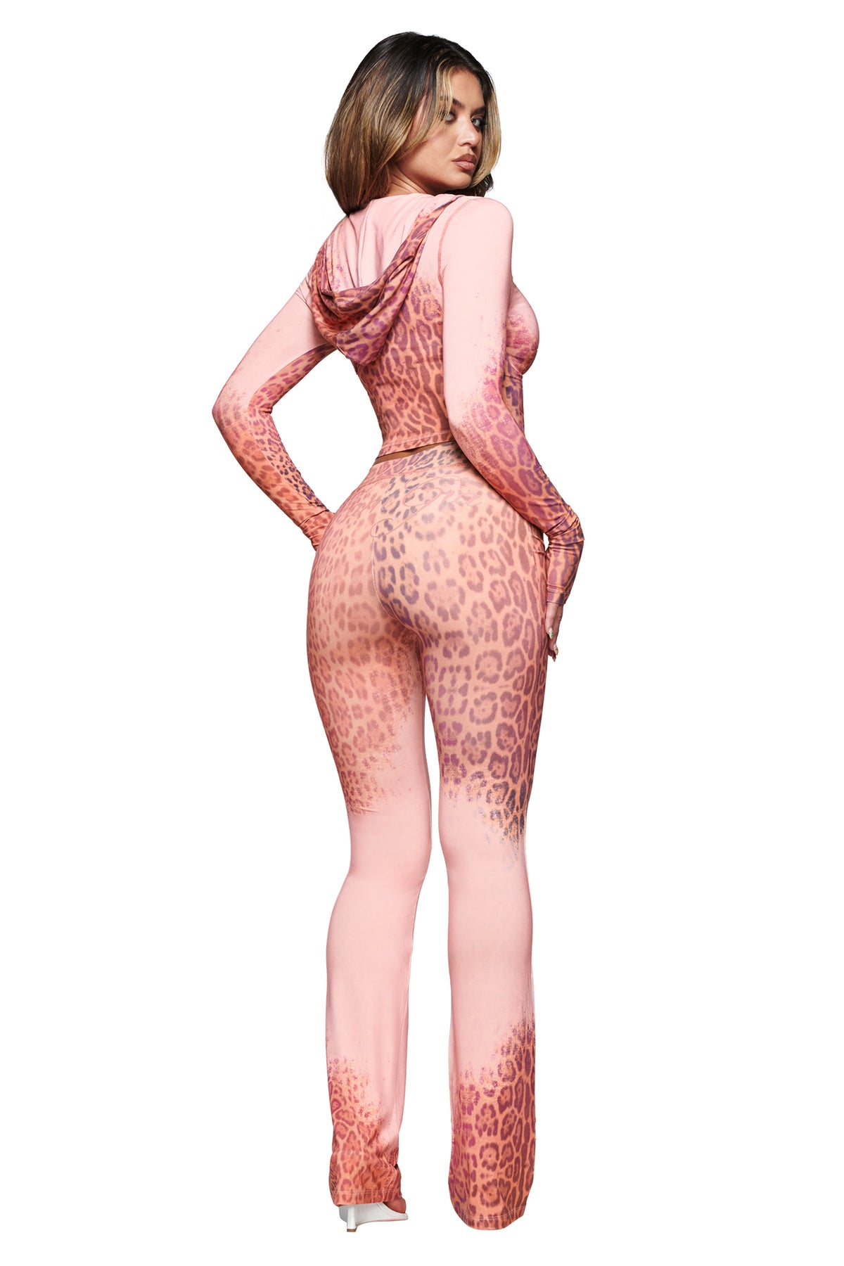 A woman faces away, wearing the I.AM.GIA BLARE TRACKPANT in Pink Faded Panthera—a pink leopard-print style with fitted legs—paired with high heels against a white background.