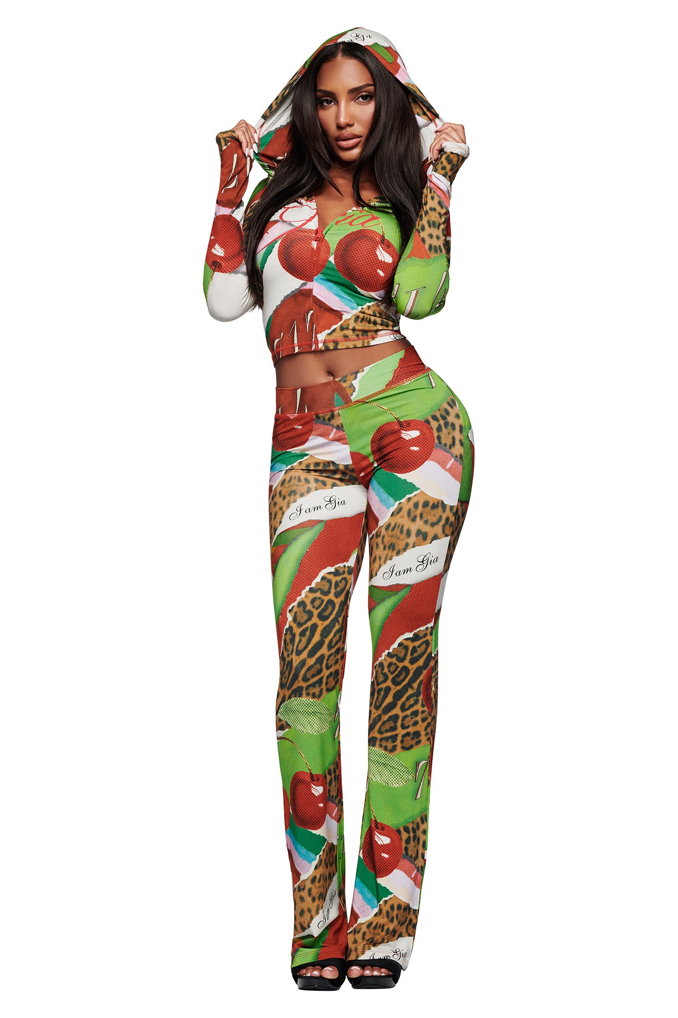 A woman models the I.AM.GIA BLARE HOODIE - WILD CHERRY, a vibrant two-piece with a hood. Featuring leopard patterns and bold script in red, green, and brown, she stands against a white background.
