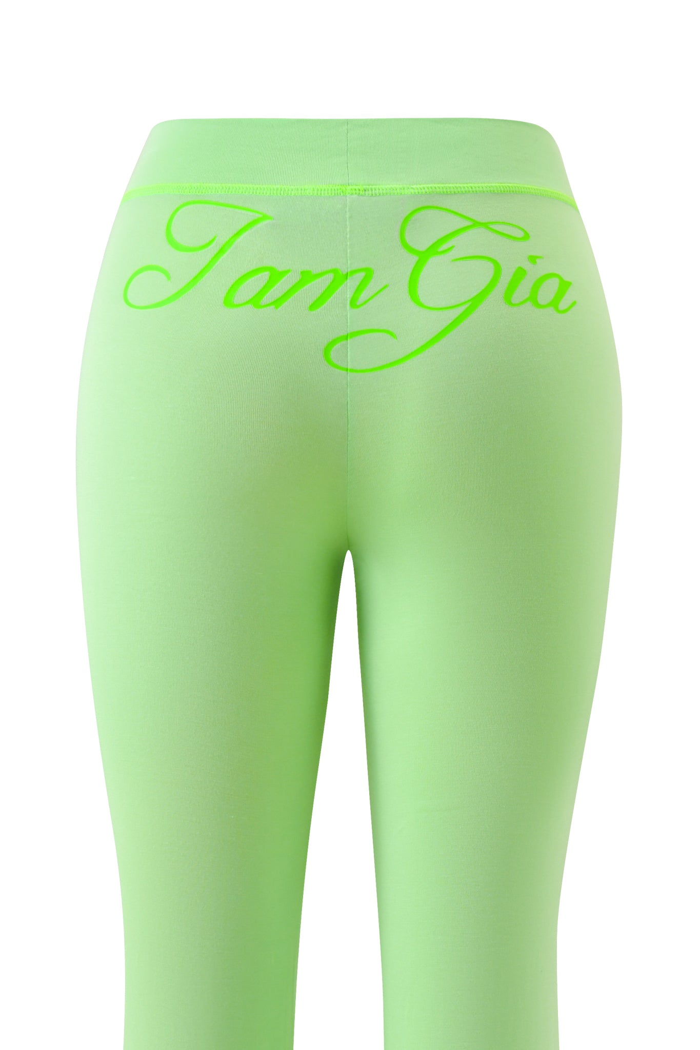The image shows the I.AM.GIA BLARE TRACKPANT - NEON GREEN from behind, highlighting bold neon green leggings with a large, cursive I.AM.GIA logo across the back waistband.