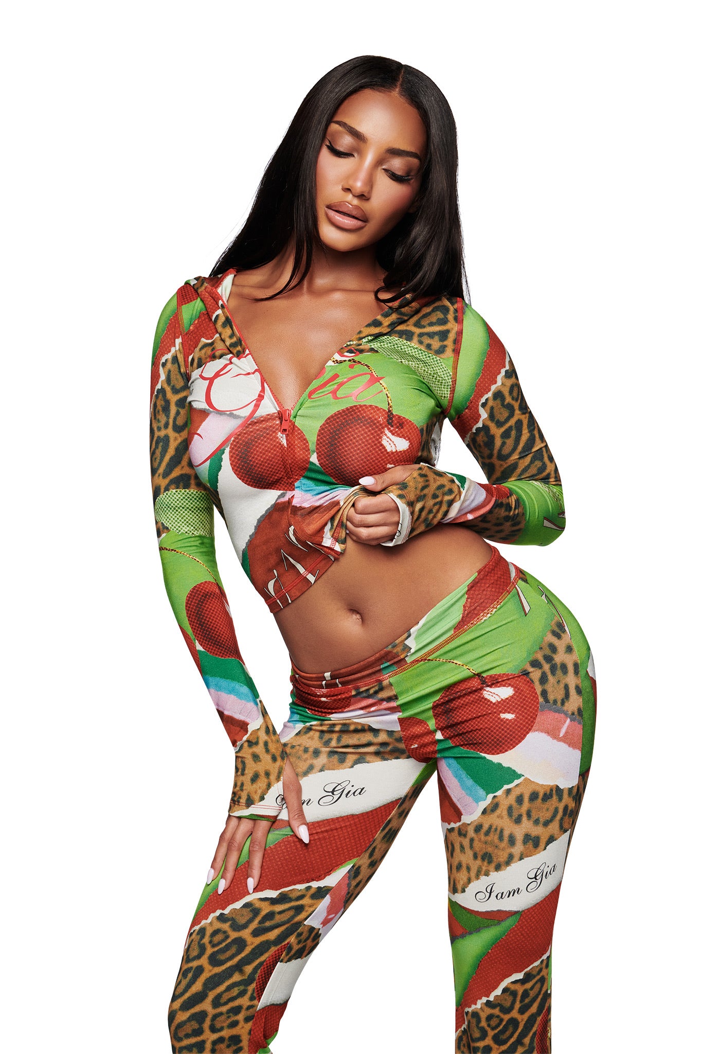 A woman poses in the I.AM.GIA BLARE HOODIE - WILD CHERRY, a colorful zip-front, long-sleeve top with green, red, and leopard print. She pairs it with matching "I am Gia" pants and wears her hair long and straight.