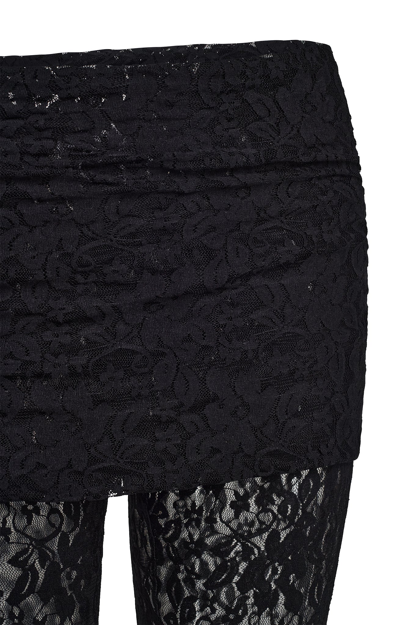 The image features a detailed view of a person dressed in the KYLEAH PANT - BLACK : LACE by I.AM.GIA. They are wearing a black lace mini skirt over black lace pants, with fabric showcasing an intricate floral pattern and semi-transparent lace. The shot captures from the waist down to part of the legs against a white background, highlighting the stylish design.