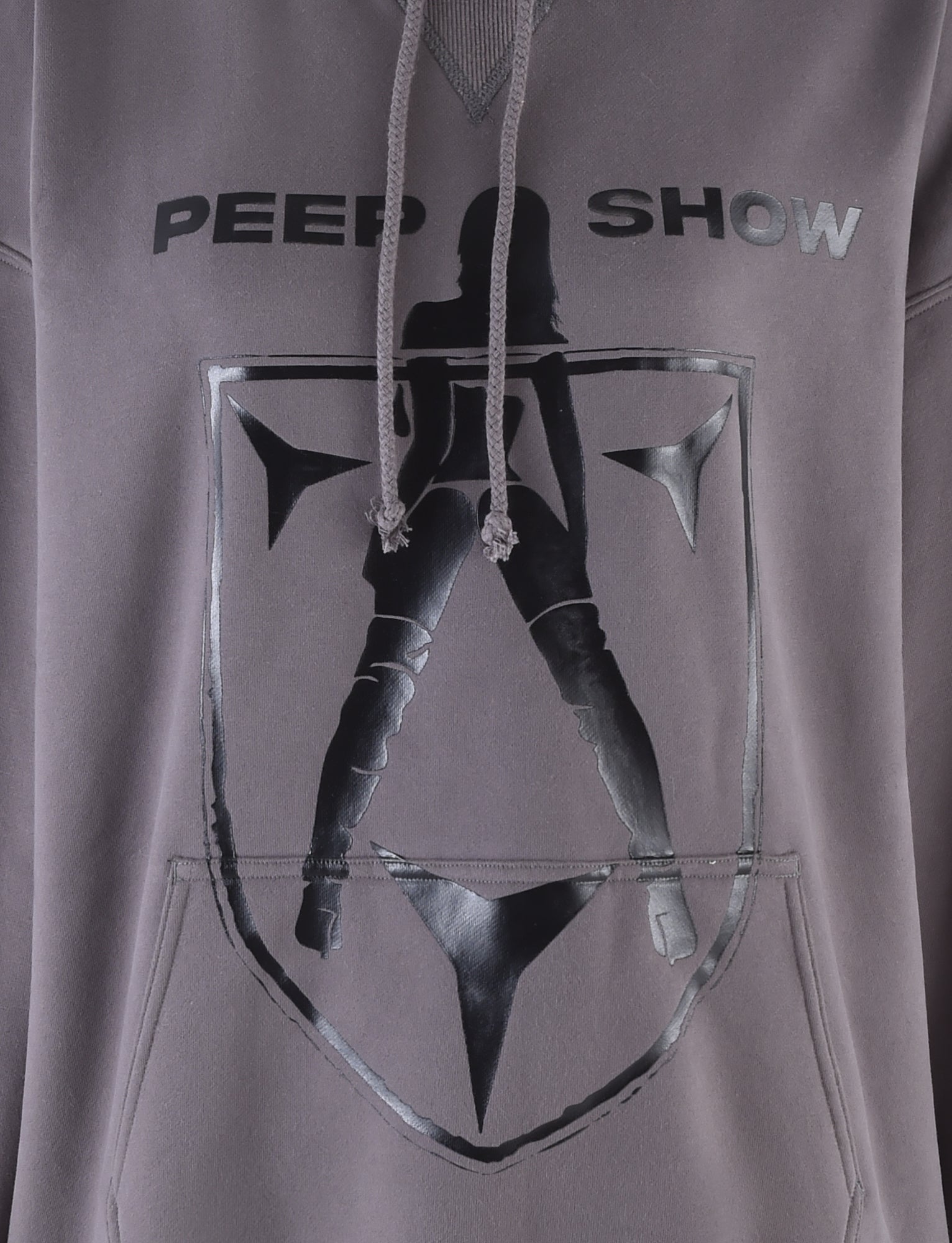 A section of the DORIAN HOODIE - GREY : CHARCOAL by I.AM.GIA is shown. The hoodie showcases the text "PEEP SHOW" above a black silhouette of a woman in high heels and thigh-high boots, encased within a black shield design. The hood's strings dangle in front of the artwork.