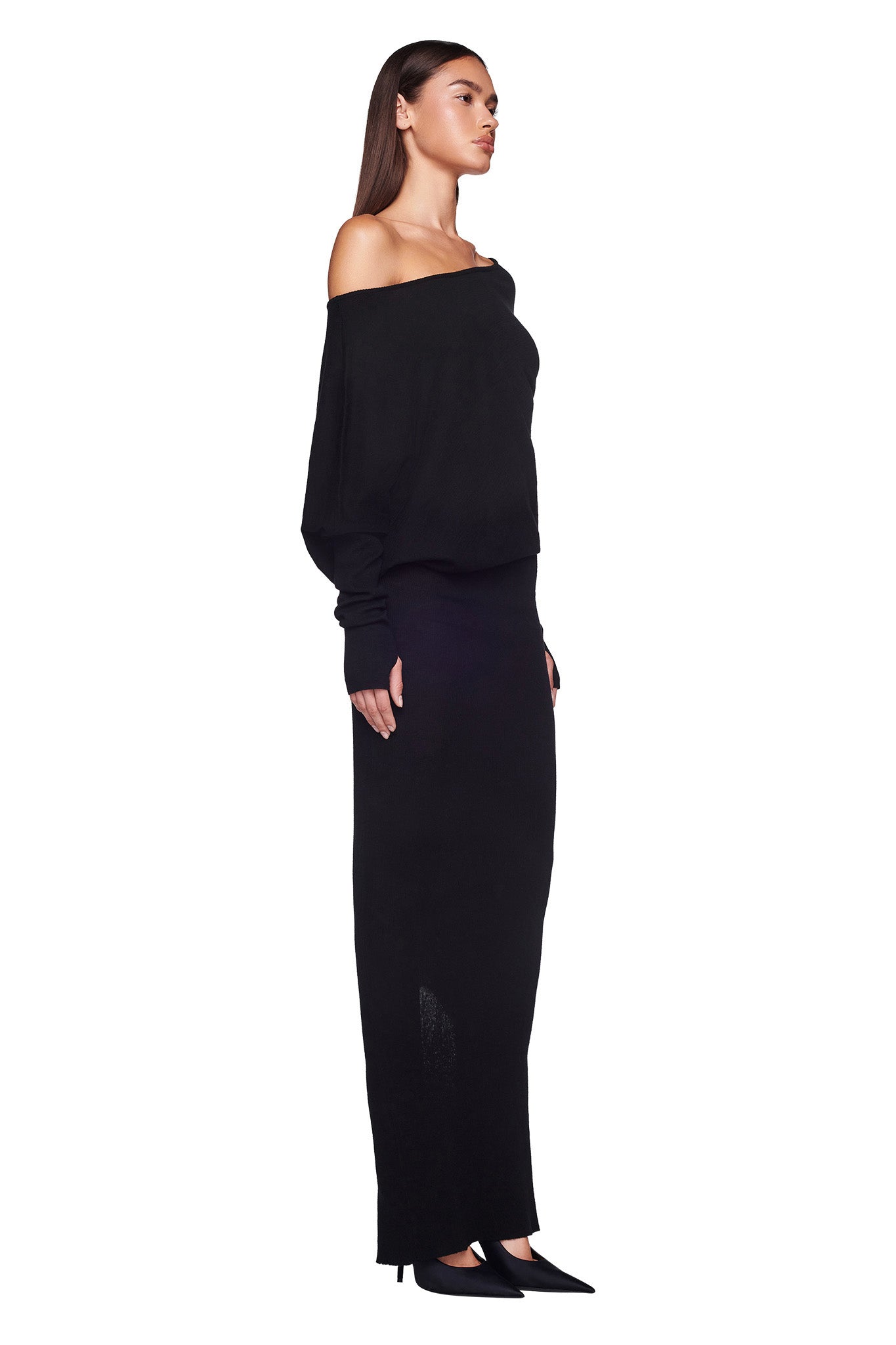 A woman is standing in profile against a white background, wearing the GISELLE MAXI DRESS - BLACK by I.AM.GIA and black pointed-toe heels. She has long, straight hair and her arms are relaxed by her sides.