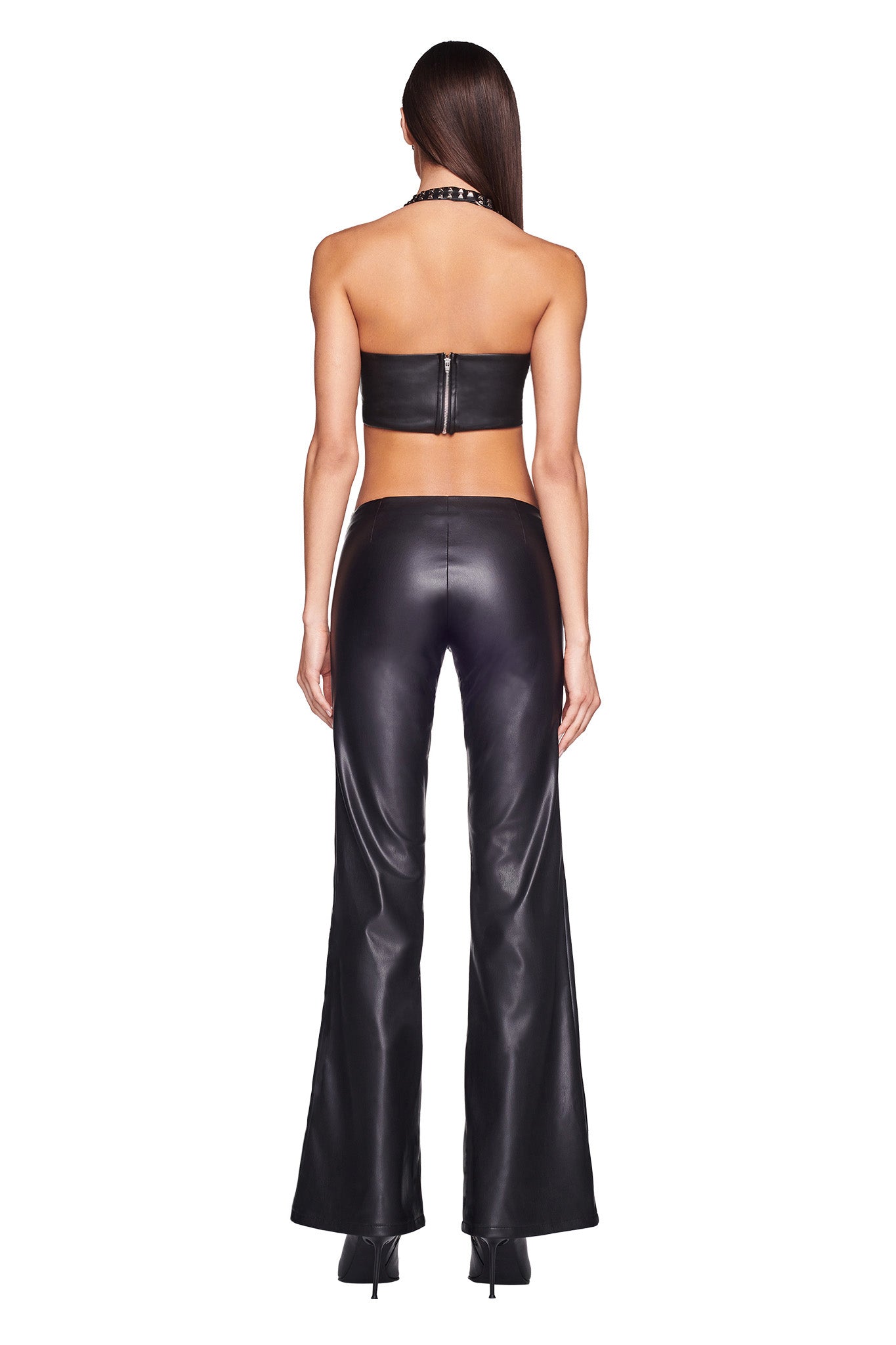 A person with long dark hair is shown from the back, wearing an I.AM.GIA black leather tube top paired with SONORA PANT - BLACK. The outfit is accessorized with black heeled boots and a black choker necklace.