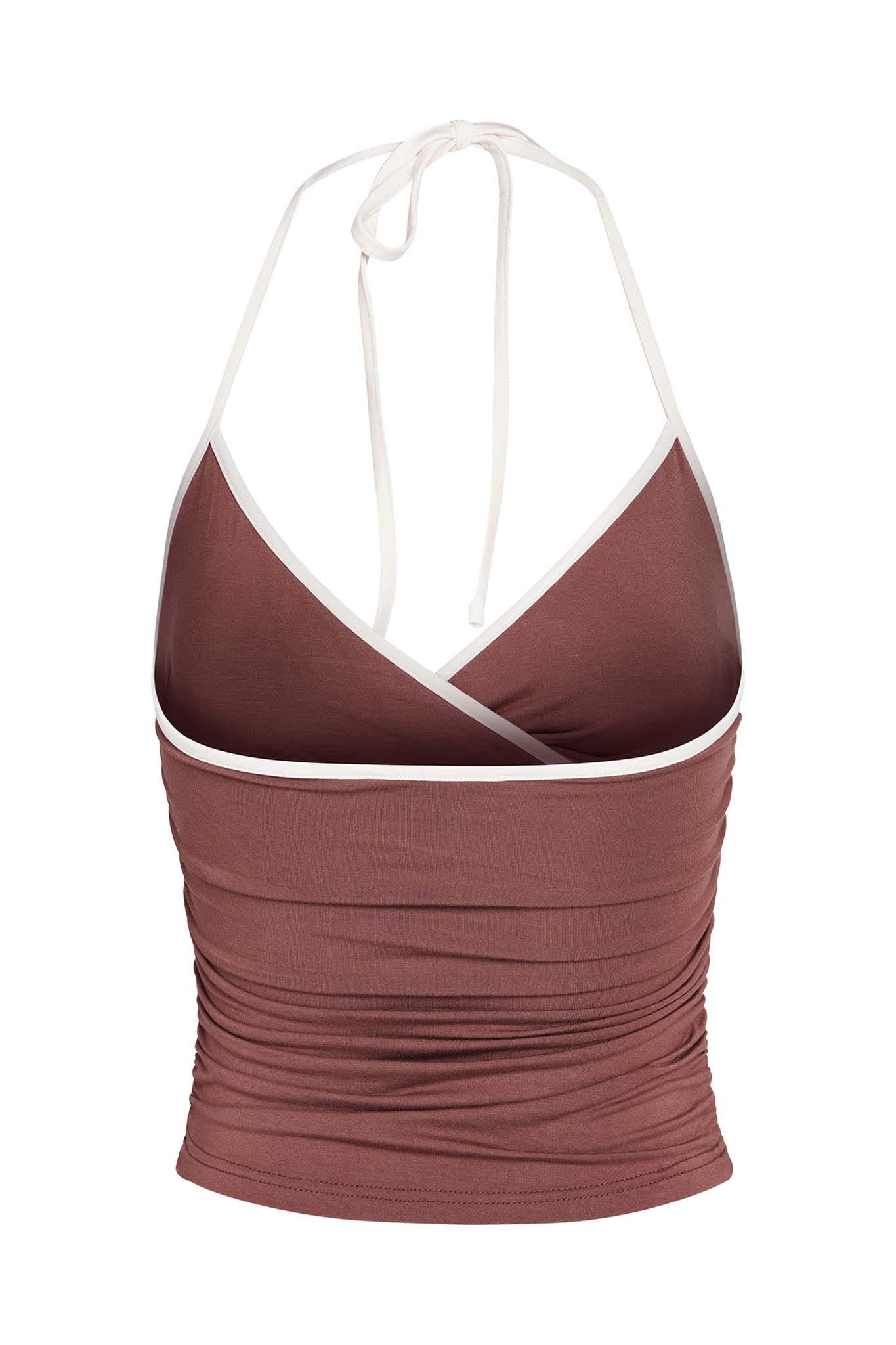 The JANNIS TANK - BROWN : CHOCOLATE from I.AM.GIA is a brown sleeveless halter top with white trim. It features a wrap-style front and ruching down the sides, creating a flattering bodycon silhouette. Made from soft bamboo fabrication, the straps tie behind the neck for an adjustable fit.