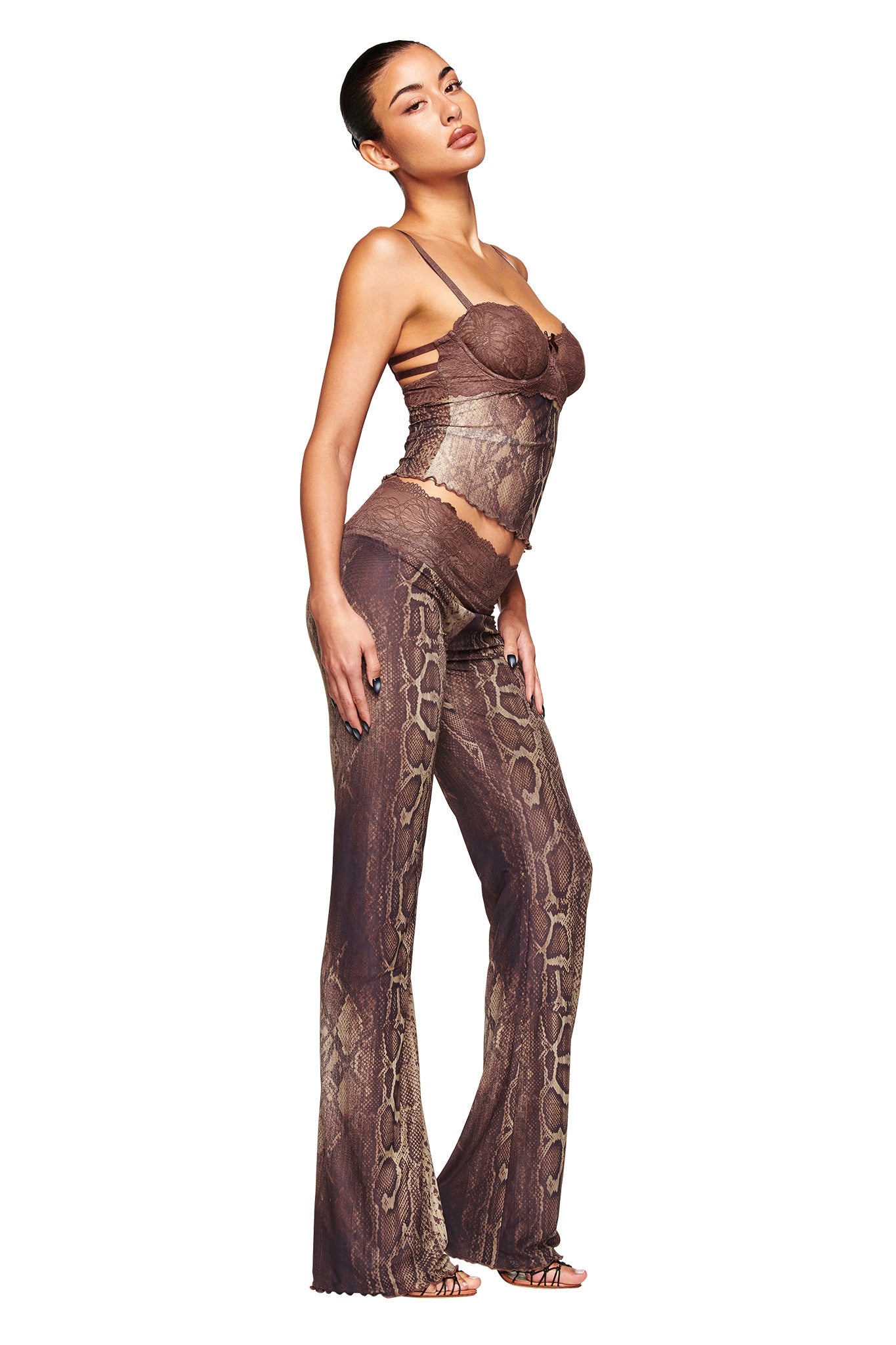 A woman poses in profile against a white background wearing I.AM.GIA's SILO PANT - SNAKE, a brown snake print flared mesh pant with a matching fitted camisole top. Her hair is slicked back.