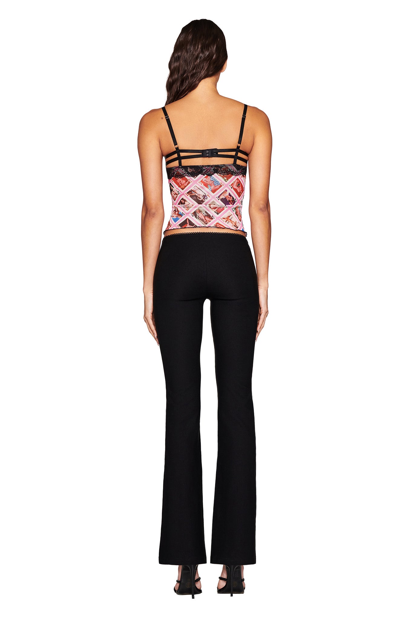 Rear view of a person with long dark hair wearing the I.AM.GIA SILO TOP - MULTI: GIA FACE CARD, featuring colorful face card prints and thin straps, paired with black flared pants against a plain white background.