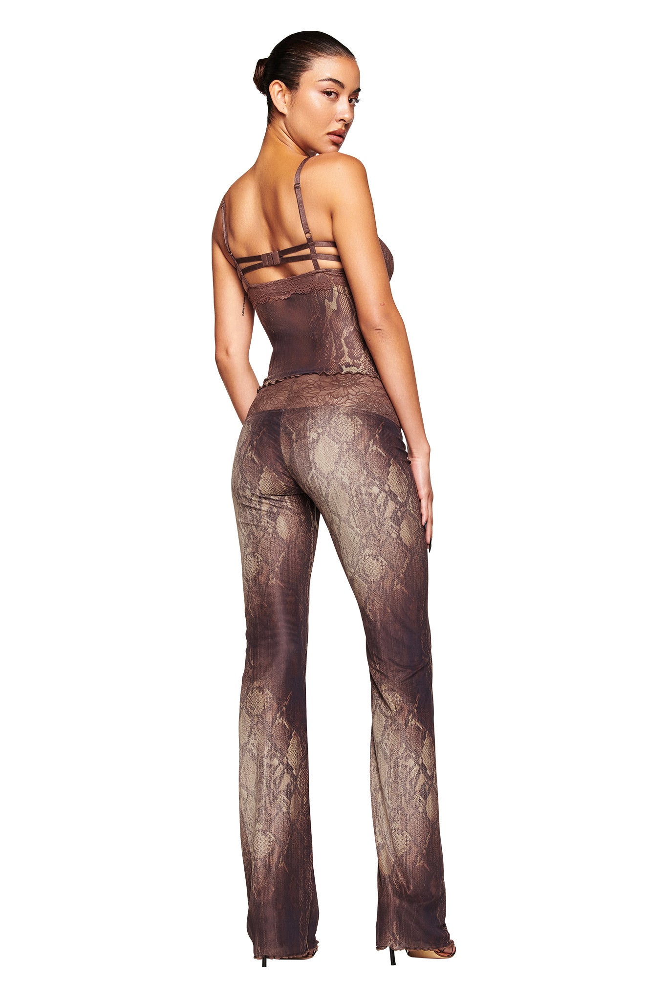 A woman with her hair in a bun faces away, looking over her shoulder. She wears I.AM.GIA's brown snake print fitted two-piece outfit with spaghetti straps and SILO PANT - SNAKE. The background is white.