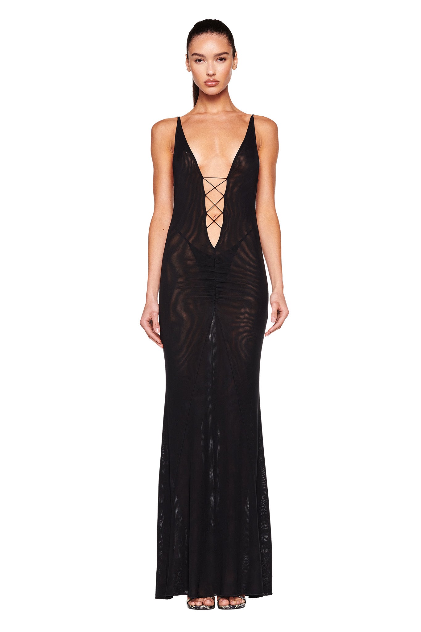 A person is wearing the I.AM.GIA MAYA DRESS in black. The long, sleeveless dress features a plunging neckline with crisscross lacing and has a form-fitting, sheer appearance. The person stands against a plain white background.
