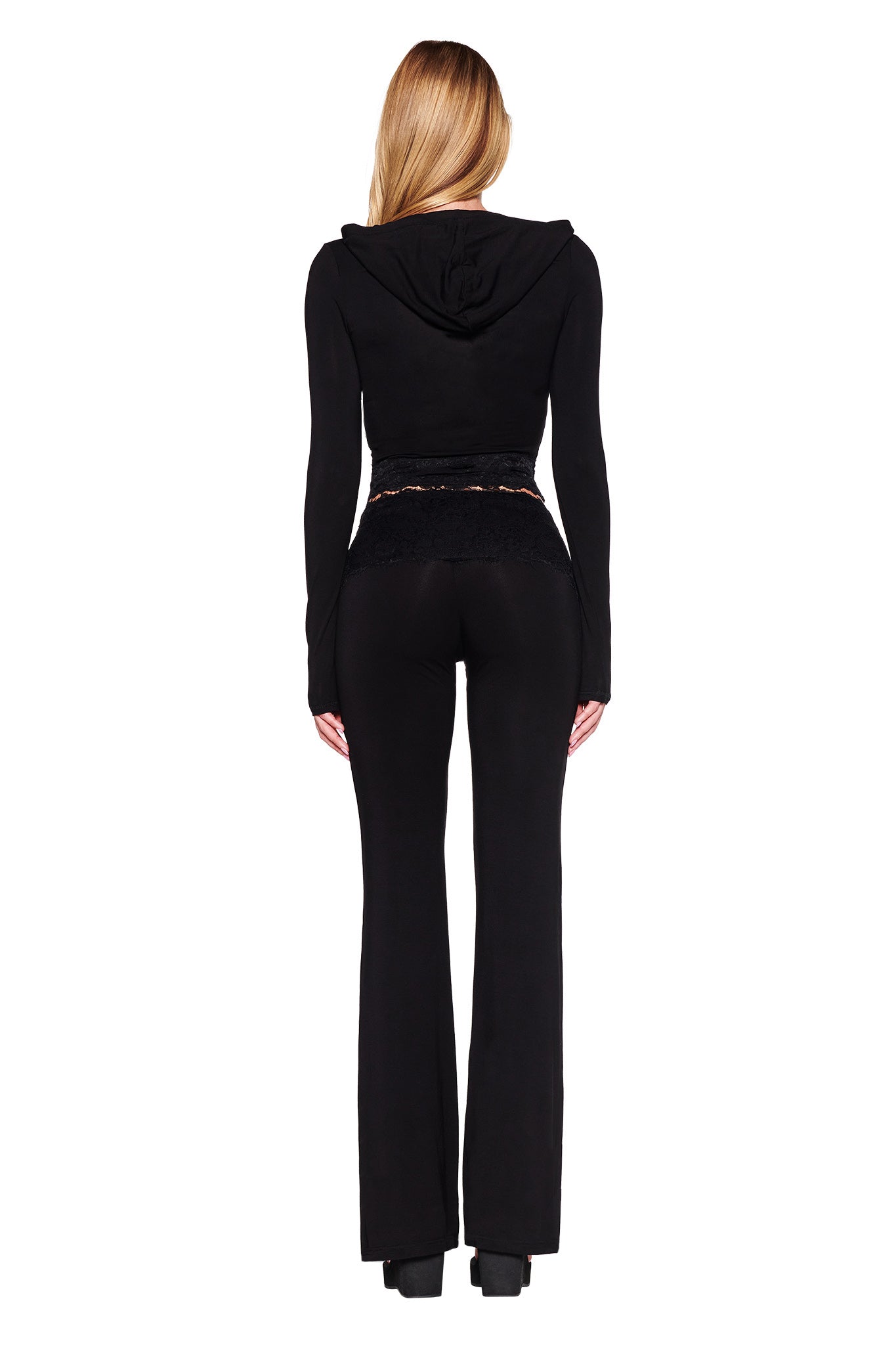 A person with long blonde hair, seen from behind, is wearing the I.AM.GIA TARSHA JACKET in True Black and matching black pants. The outfit features lace detailing around the waist and the I.AM.GIA logo. They are standing against a white background.