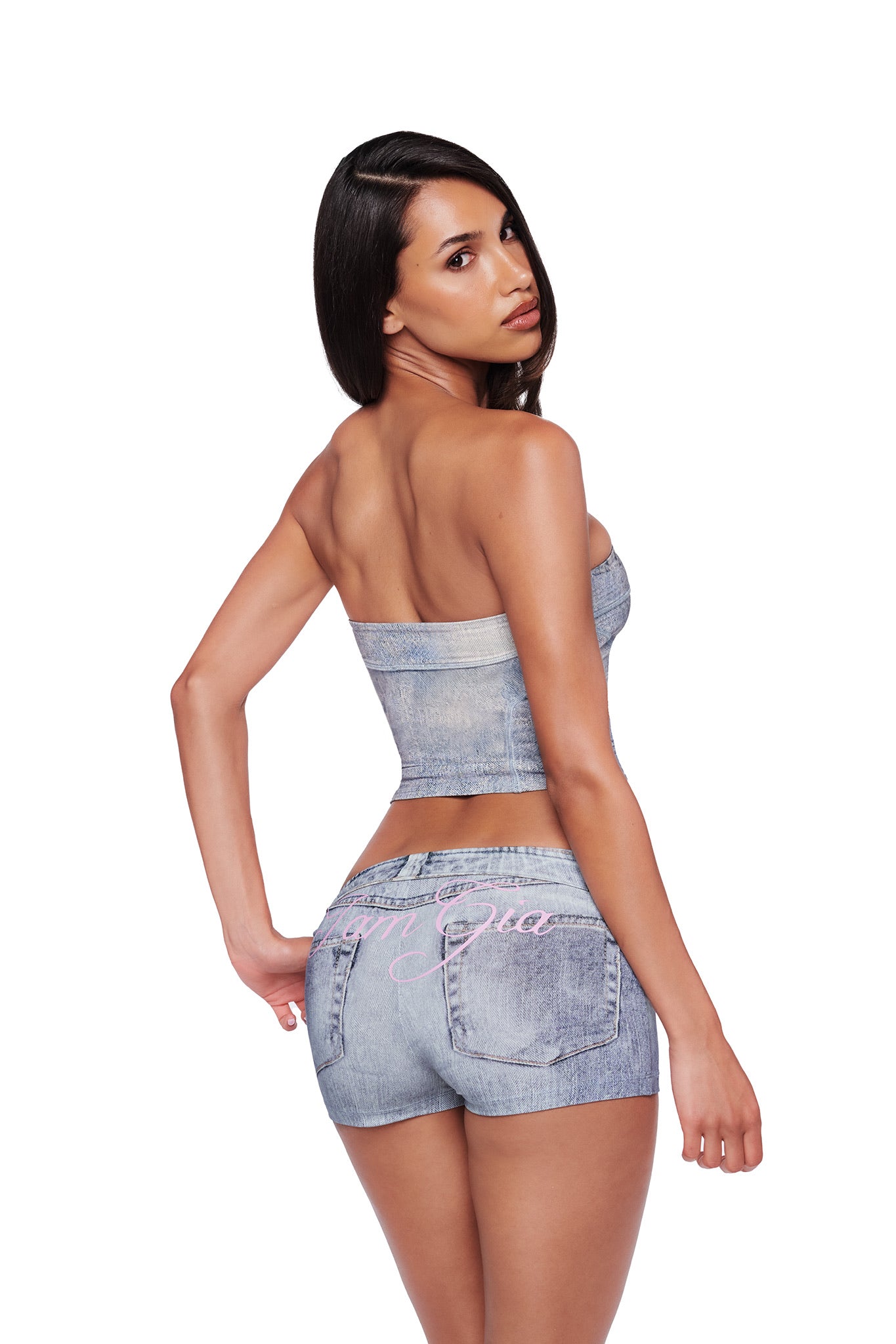 A woman wearing a denim tube top and I.AM.GIA BLARE SHORT - DENIM TROMPE L’OEIL stands against a white background, looking over her shoulder toward the camera.