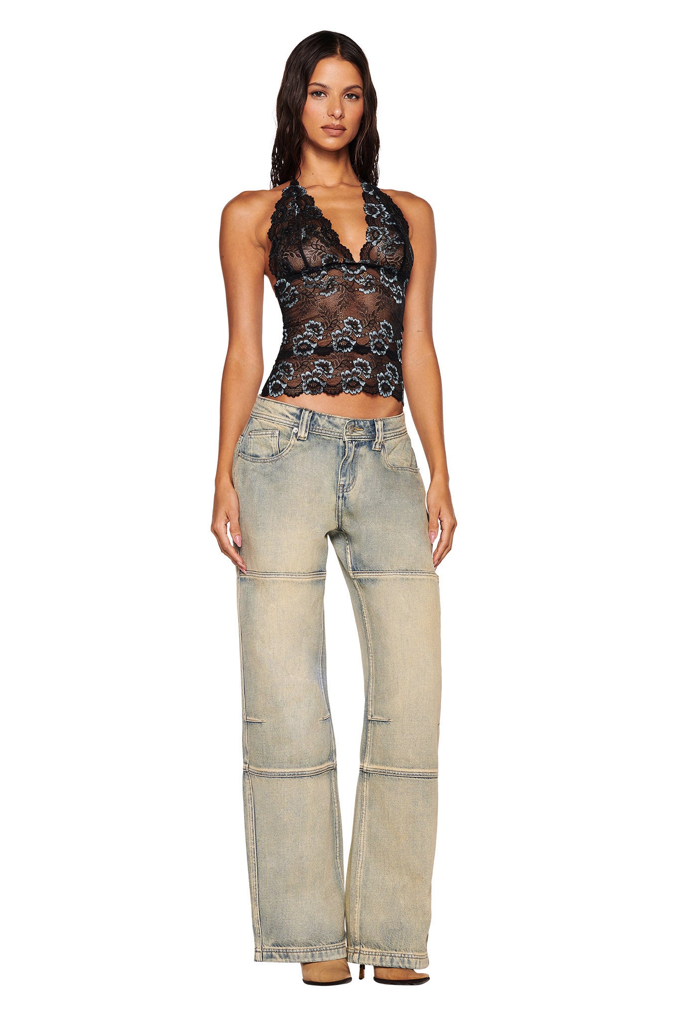 A woman with long, wavy dark hair and neutral makeup faces forward in a black lace halter top and I.AM.GIA MISTY JEAN - TAN 2.0, light-washed wide-leg jeans with visible seams and a low-rise waist, posing against a plain white background.