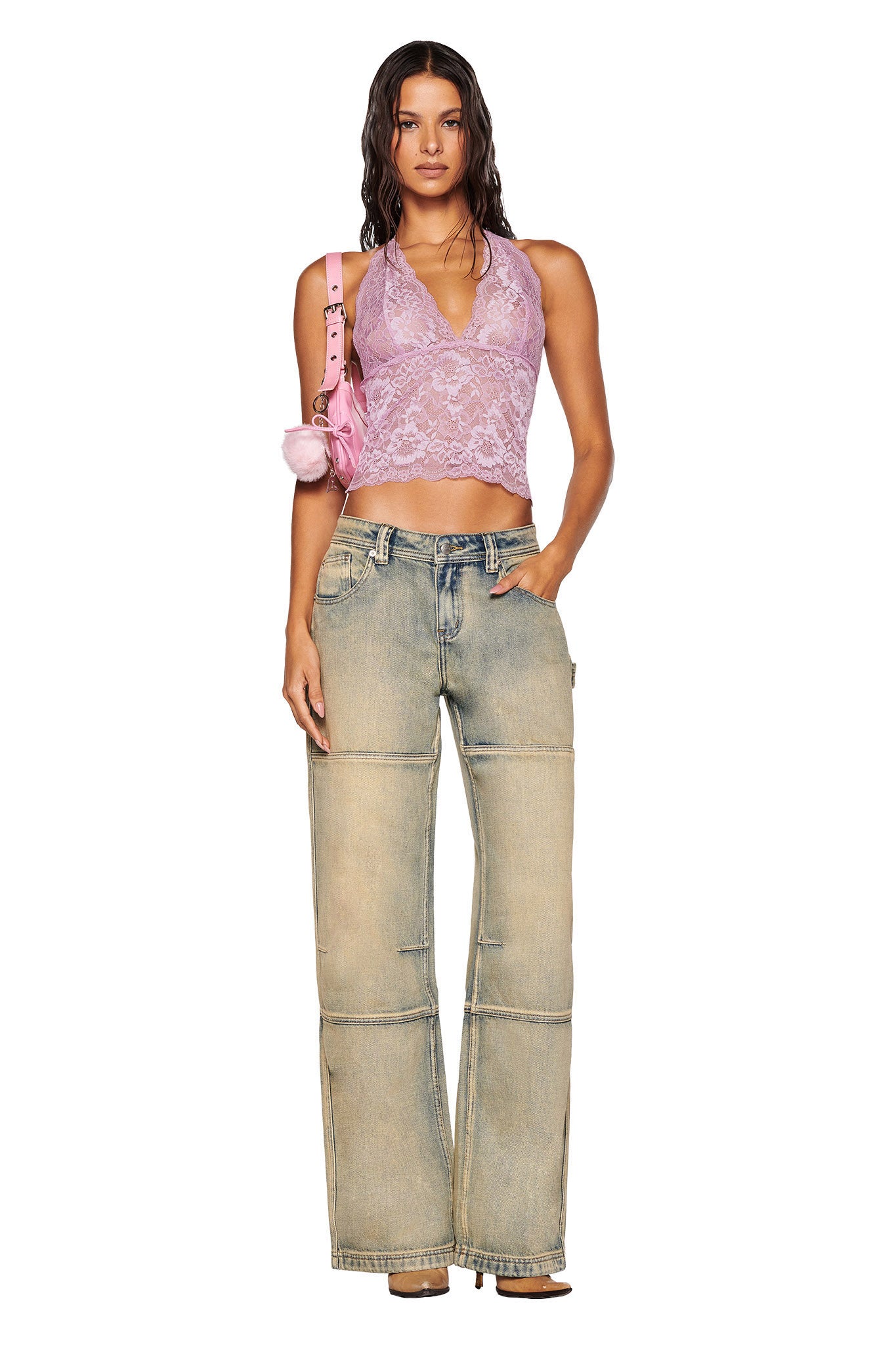 A person with long, wet hair stands facing the camera. They wear a lilac GEM HALTER TOP by I.AM.GIA, along with loose faded jeans, and hold a pink handbag over their shoulder. Their hand is in their pocket, and they are wearing high heels.