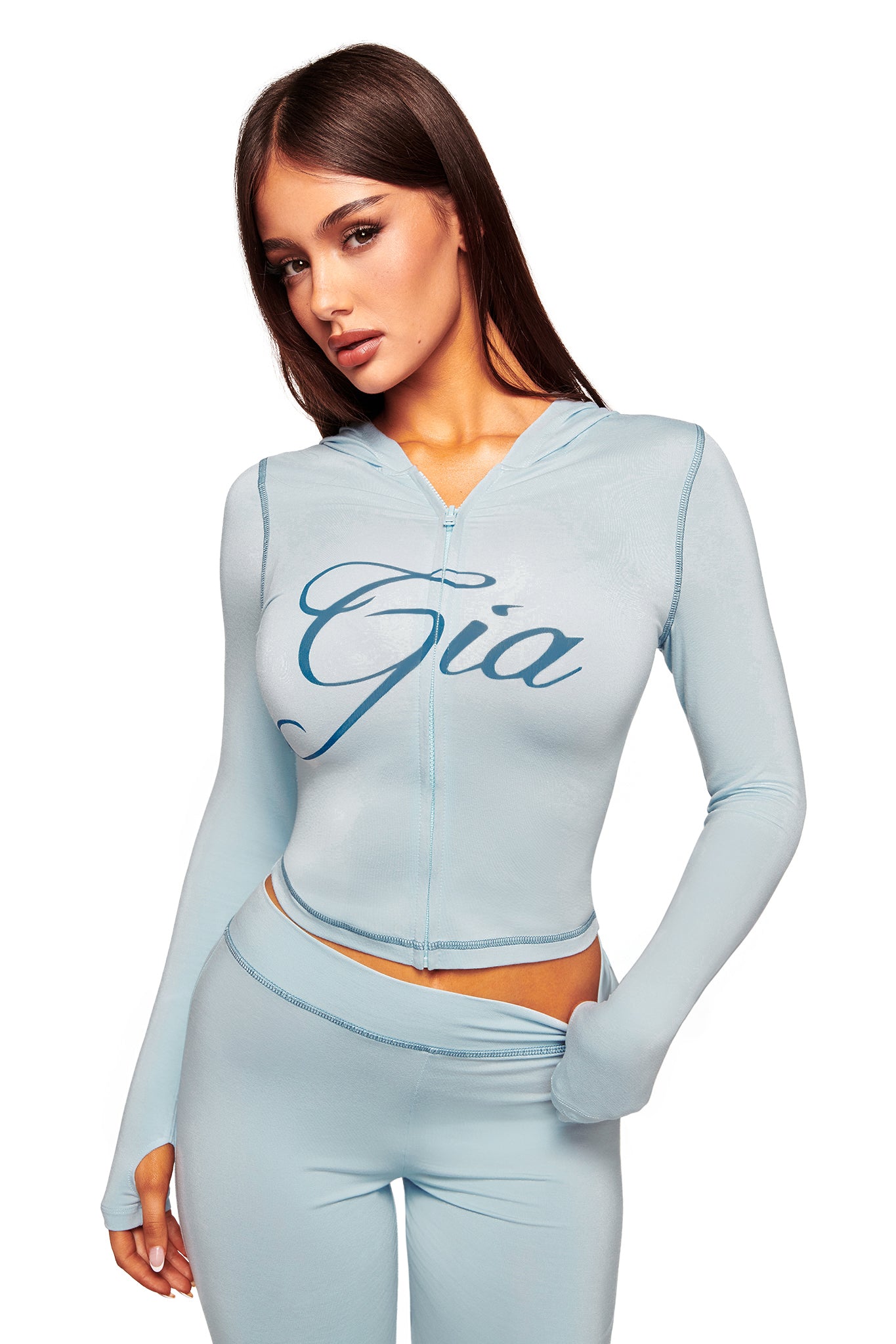 A woman poses against a white background in a fitted I.AM.GIA BLARE HOODIE - BLUE : BABY BLUE with "Gia" on the front and matching leggings.