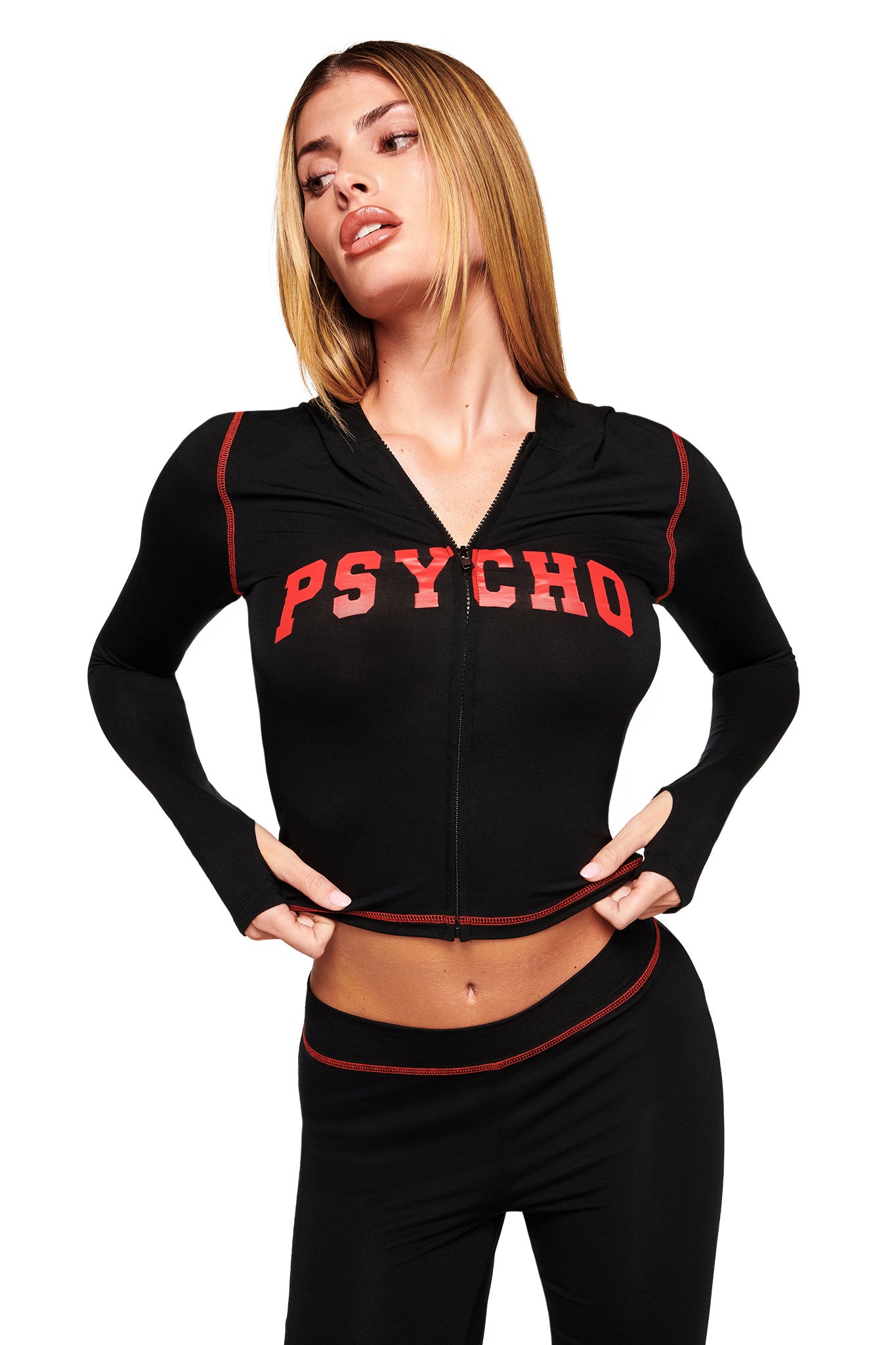 A woman with straight blonde hair confidently poses in the I.AM.GIA BLARE HOODIE - BLACK PSYCHO with red “PSYCHO” lettering and red piping, paired with matching black pants, against a white background.