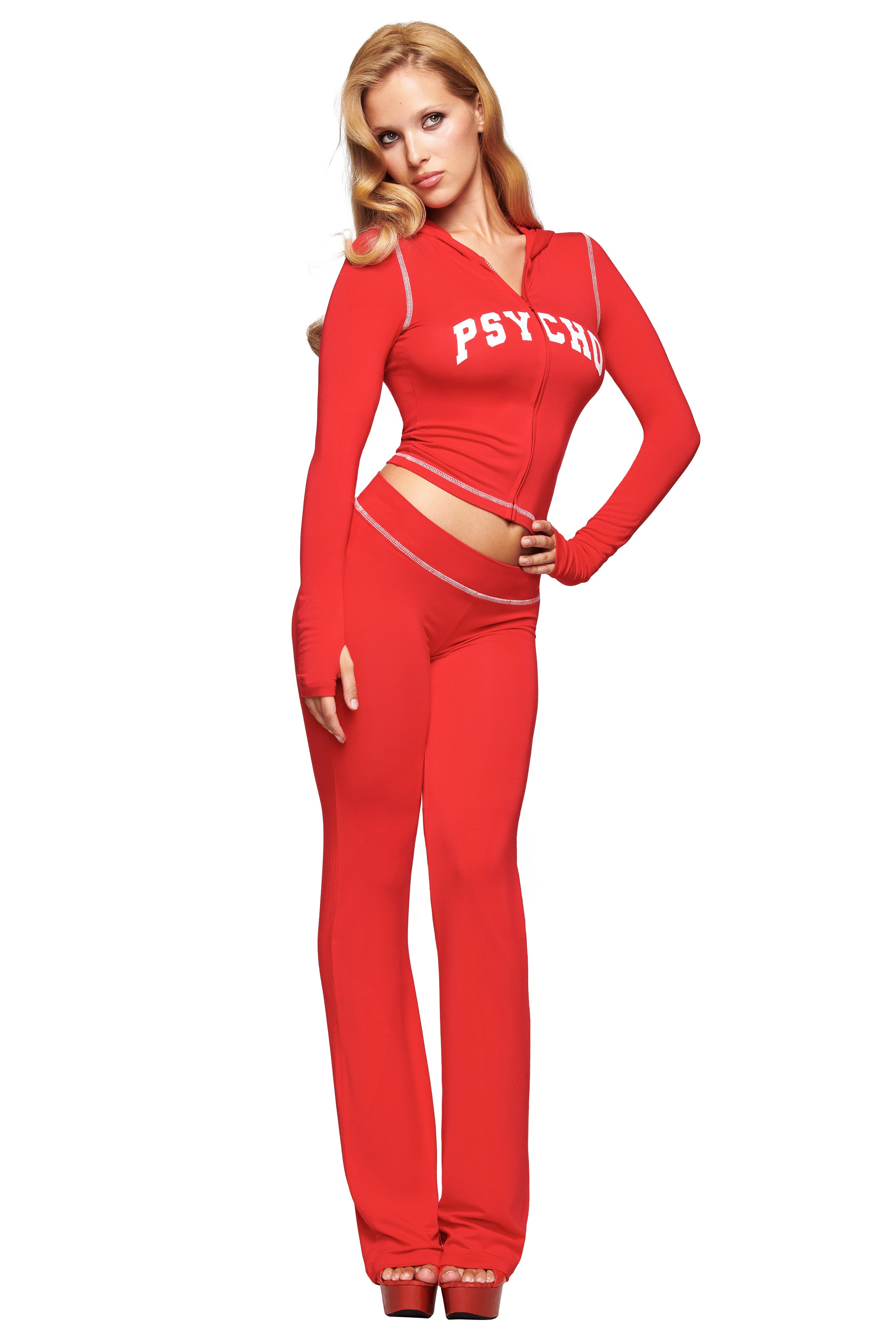 A woman with long blonde hair poses confidently in I.AM.GIA's BLARE TRACKPANT - RED : PSYCHO : SALSA, paired with a matching zip-up hoodie reading "PSYCHO," against a plain white background.