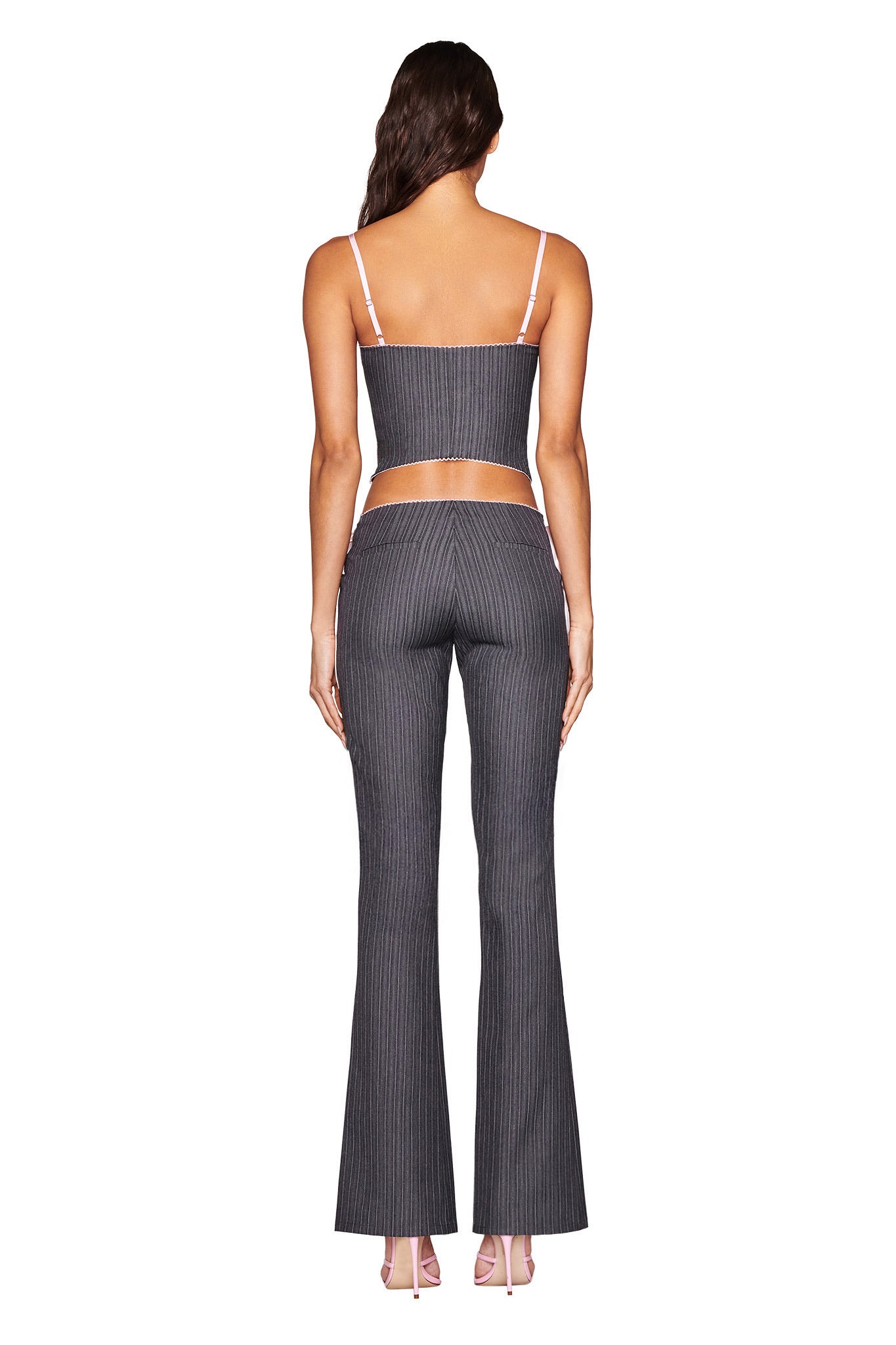 Facing away, the person wears I.AM.GIA's FLORIAN CORSET - GREY in a tailored pinstriped two-piece featuring a sleeveless crop top and high-waisted flared pants, set against a plain white background.