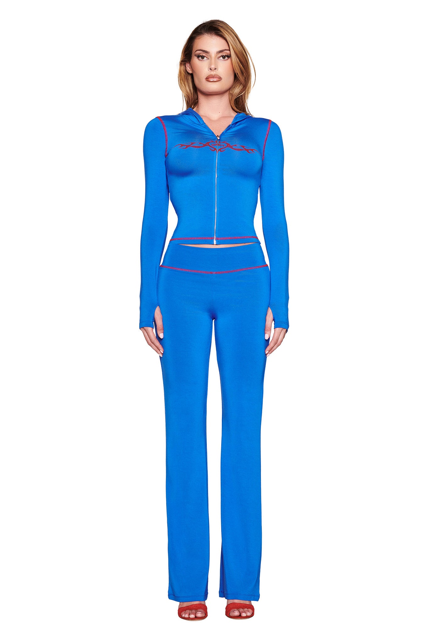 Facing forward, a person wears an I.AM.GIA BLARE HOODIE in royal blue with red trim, subtle chest design, and matching pants. Their look is completed with red open-toe shoes against a plain white background.