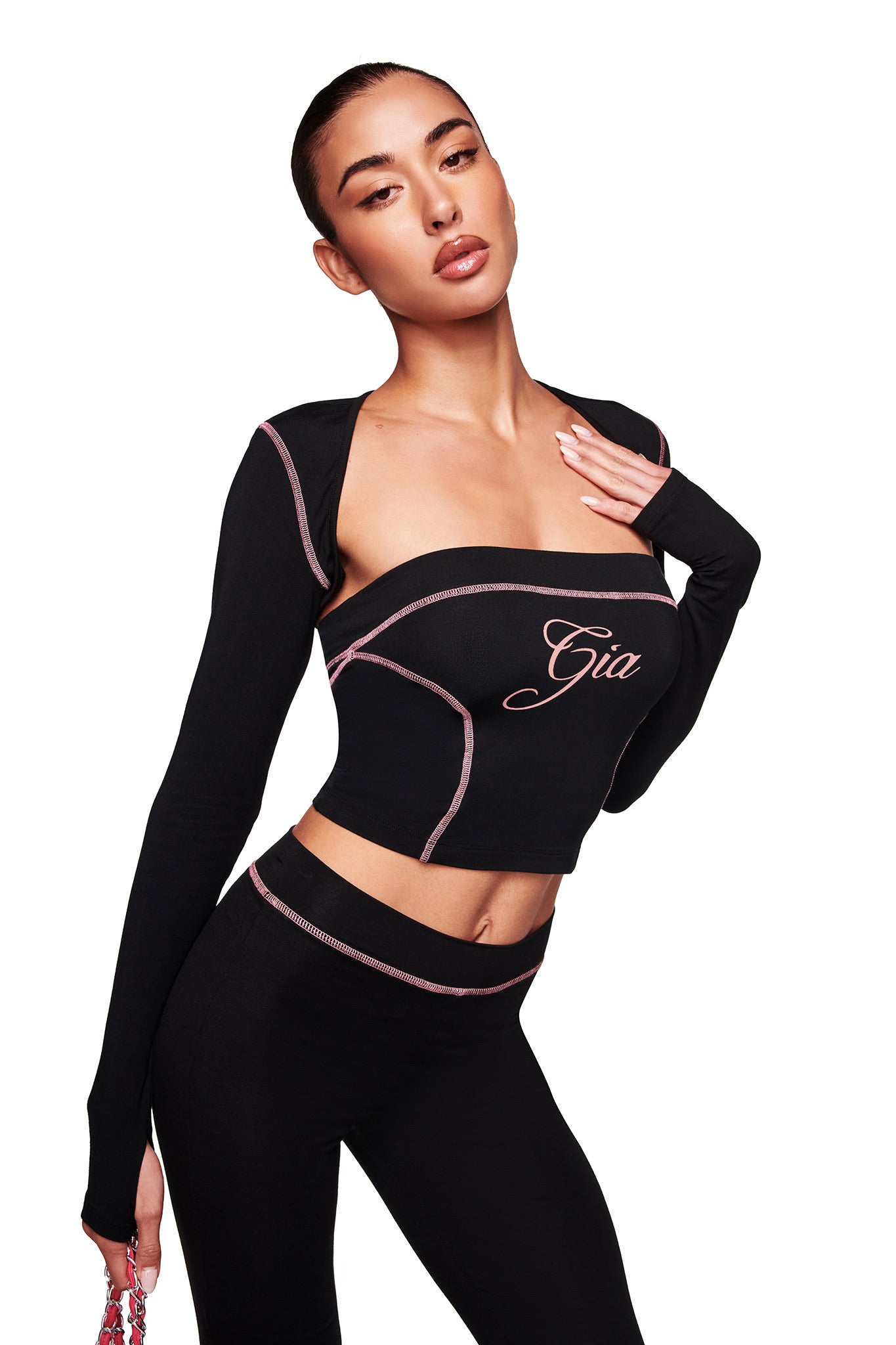 A woman models the I.AM.GIA BLARE BOOB TUBE in black, a fitted bamboo piece with sporty princess seams and pink trim, "Gia" embroidered on the chest. She poses against a white background, holding a small pink accessory.