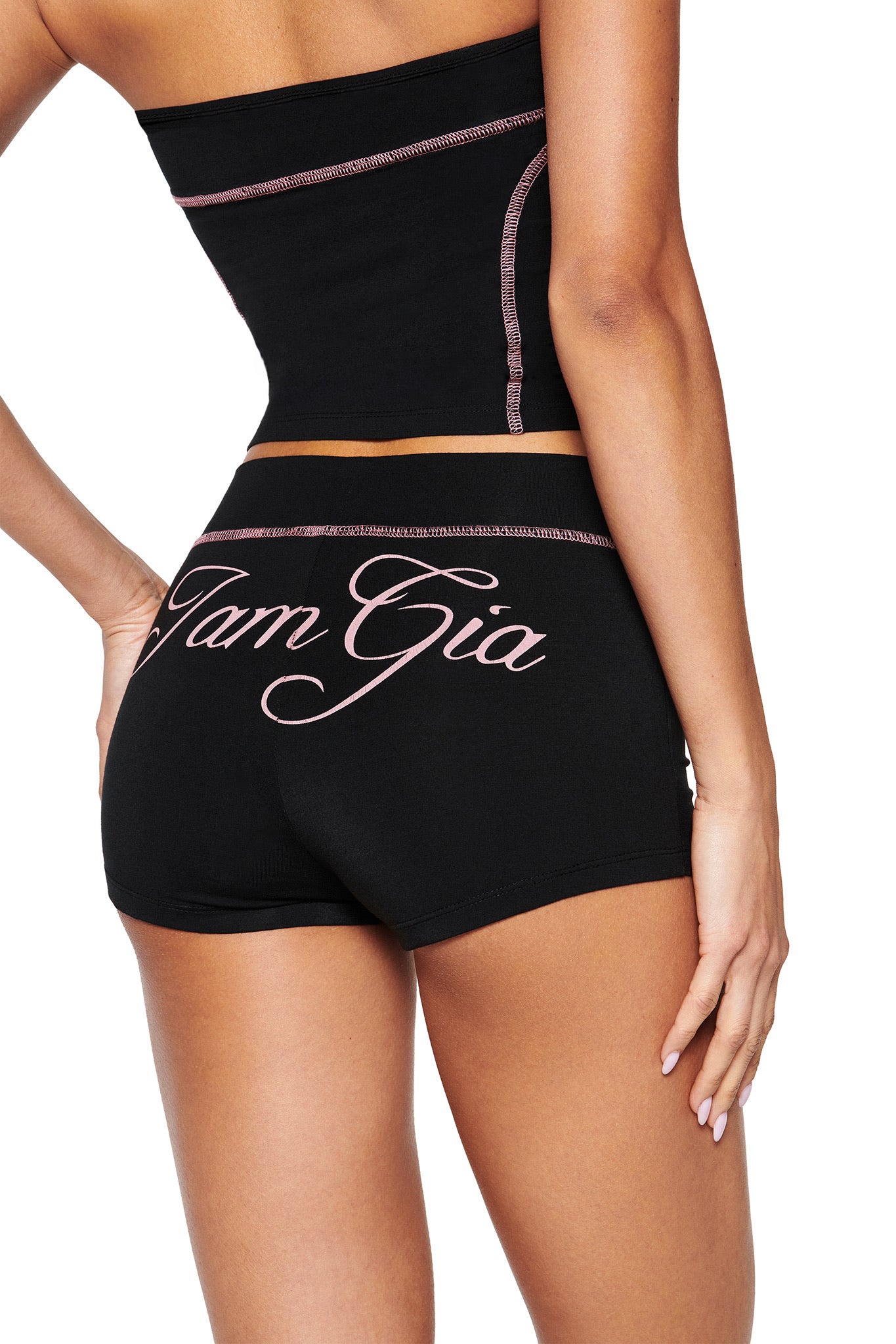 Back view of a person in a sleek black tube top and BLARE SHORT - BLACK by I.AM.GIA. "Tam Gia" is displayed in pink script, with the bodycon fit accentuating matching pink stitching for style and comfort.