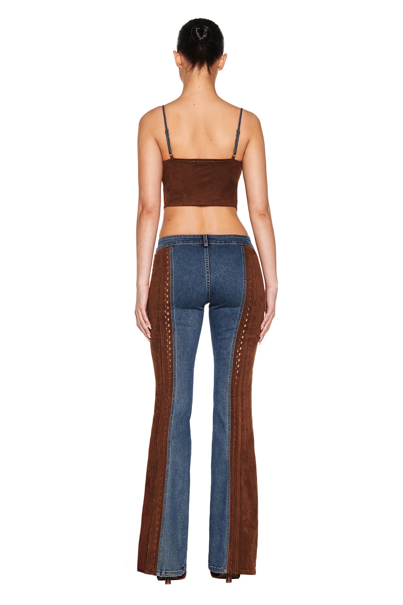 Against a white backdrop, a person faces away from the camera, wearing an I.AM.GIA sleeveless brown cropped top and FORREST PANT - BLUE: MEDIUM WASH jeans with vintage effect and brown suede contrast panels. Their hair is styled in a bun.
