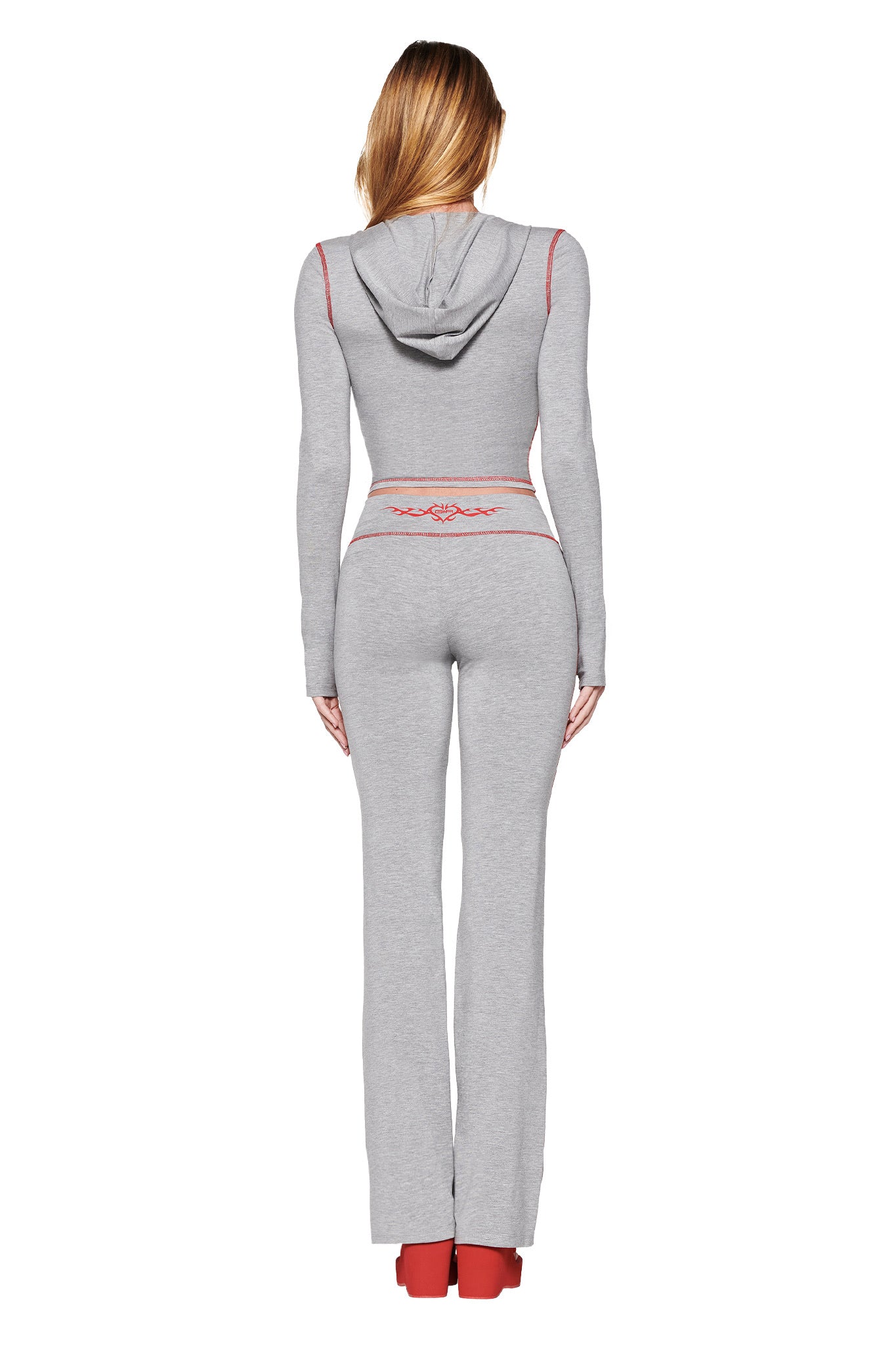 A person is seen from the back wearing I.AM.GIA's Blare Hoodie in Dove Grey, paired with matching flared pants. This tracksuit features red accents, long sleeves, and a hood, highlighted by the GIA Flame logo on the back.