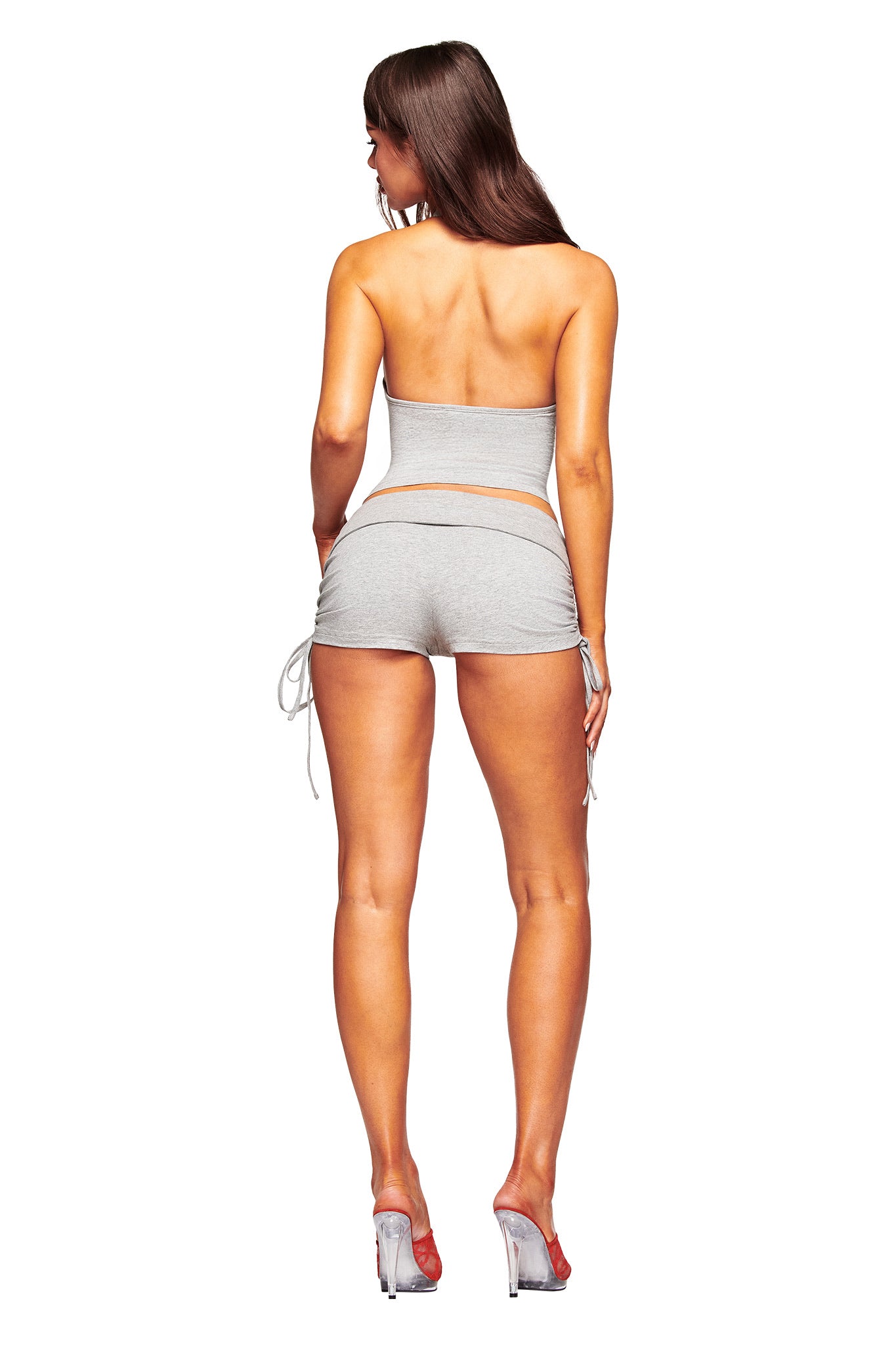 A woman with long brown hair faces away, wearing the I.AM.GIA ROWAN TOP in heather grey with matching side-tie shorts and clear heels, set against a plain white background.
