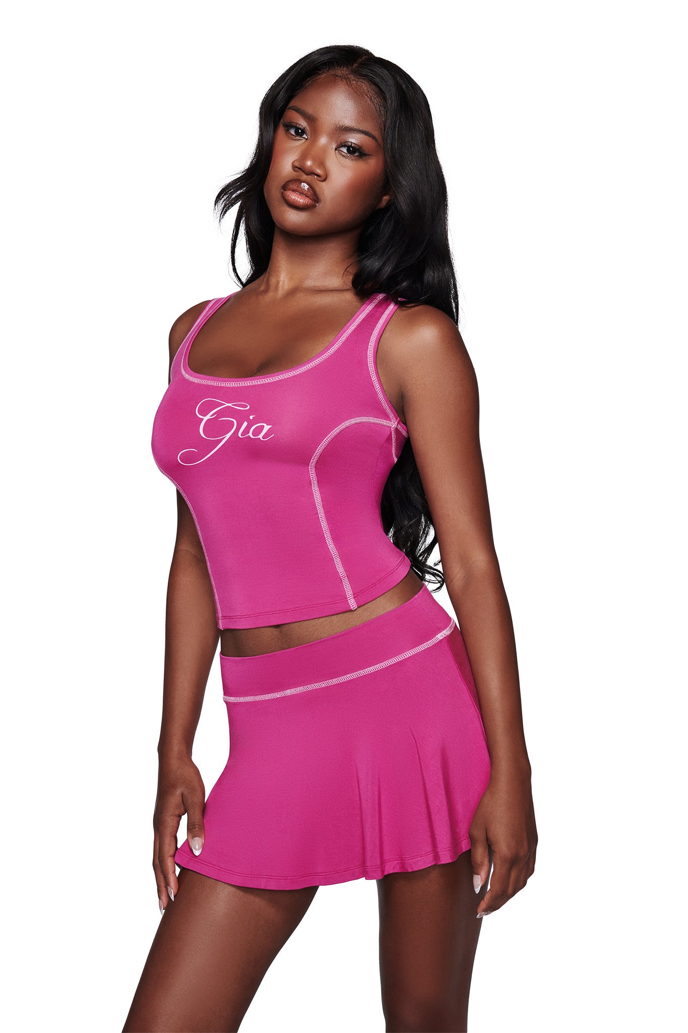 A woman with long black hair wears the I.AM.GIA BLARE TANK in raspberry and a matching skirt, standing confidently against a plain white background.