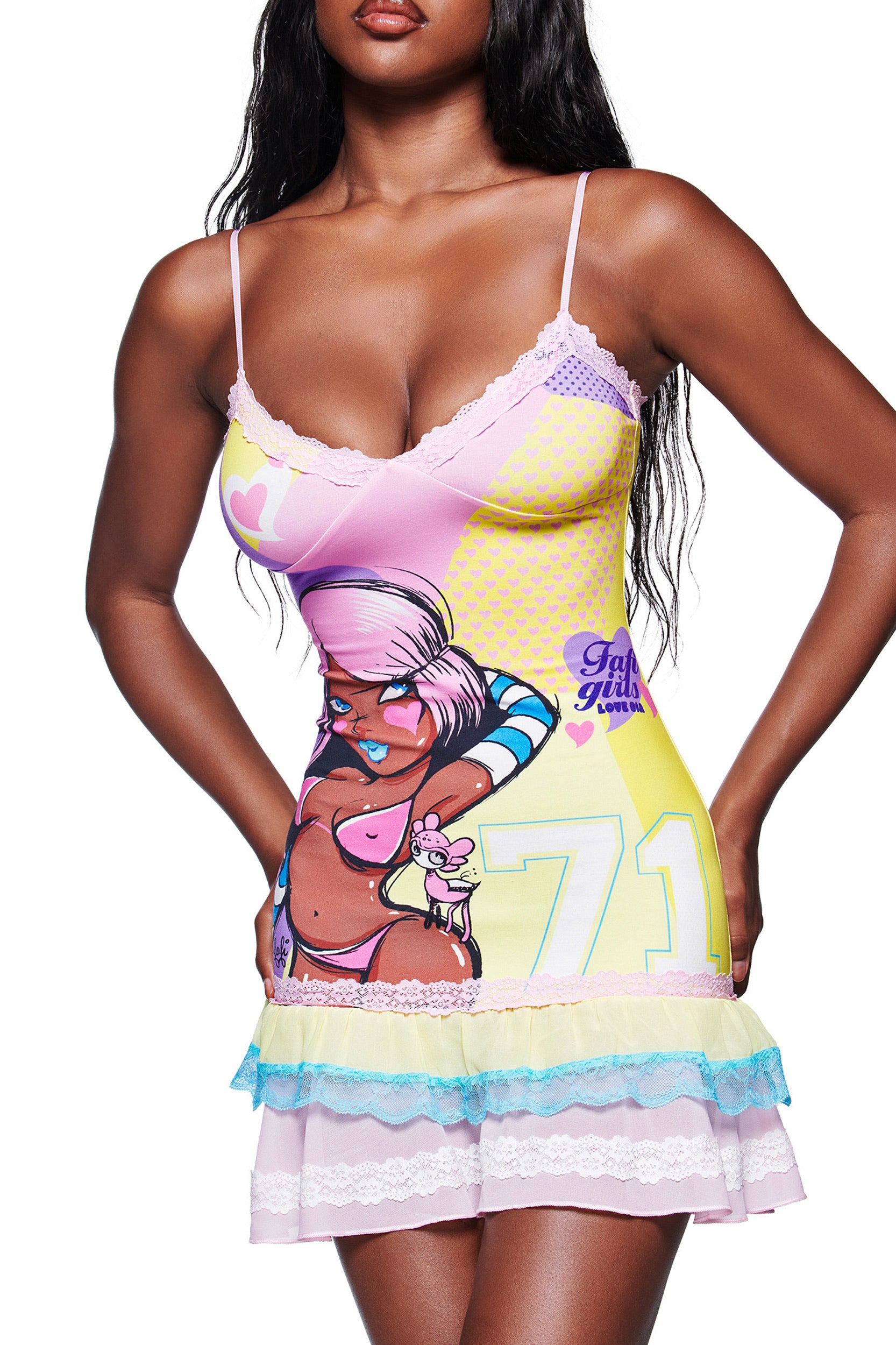 A woman wears the I.AM.GIA FAFI MINI DRESS - YELLOW, a colorful stretch jersey mini dress with an exclusive cartoon-style print, lace trim, and pastel ruffle details. Her face is not visible.