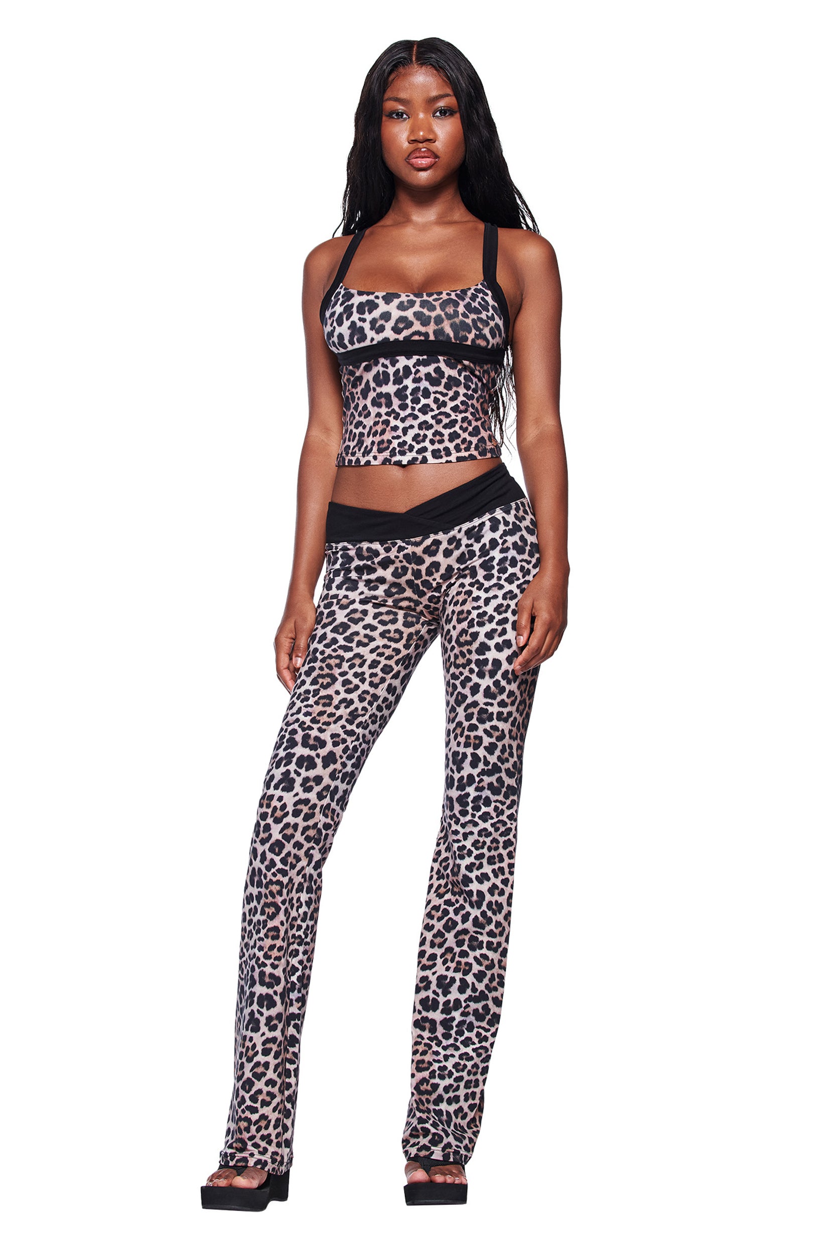 A woman with long straight hair and a neutral expression wears the I.AM.GIA BLARE HALTER STRAP TOP - LEOPARD with matching flared pants and black platform sandals, facing forward against a white background.