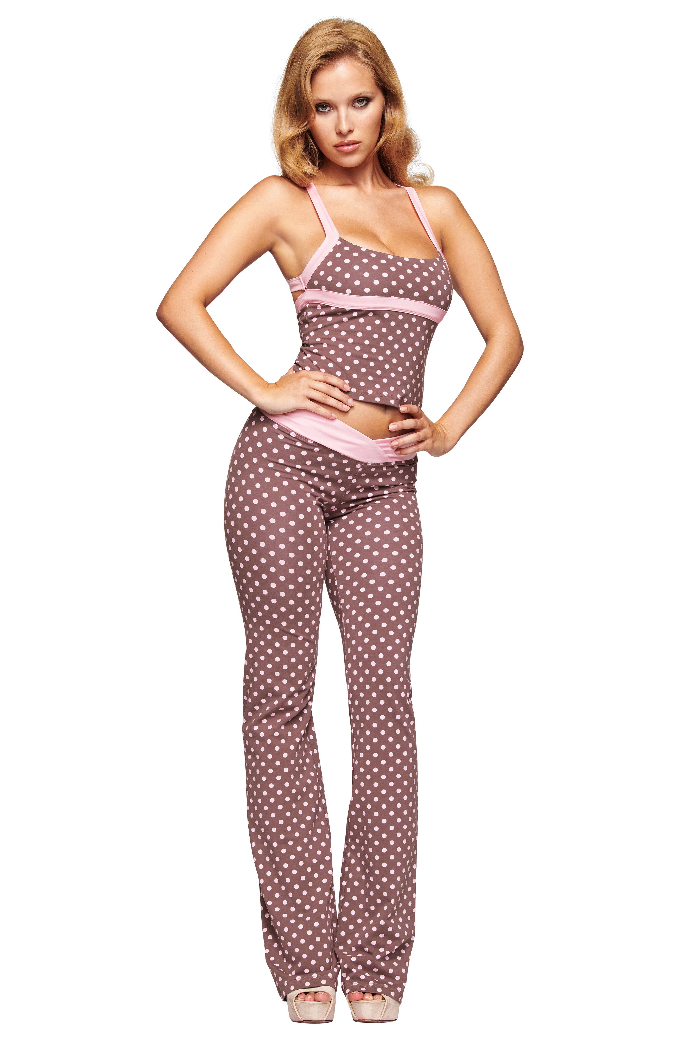 A woman stands with hands on hips, wearing the I.AM.GIA BLARE CROSSOVER PANT in Pink Chocolate, featuring a flared leg and paired with a matching polka dot sleeveless top and light-colored high heels.