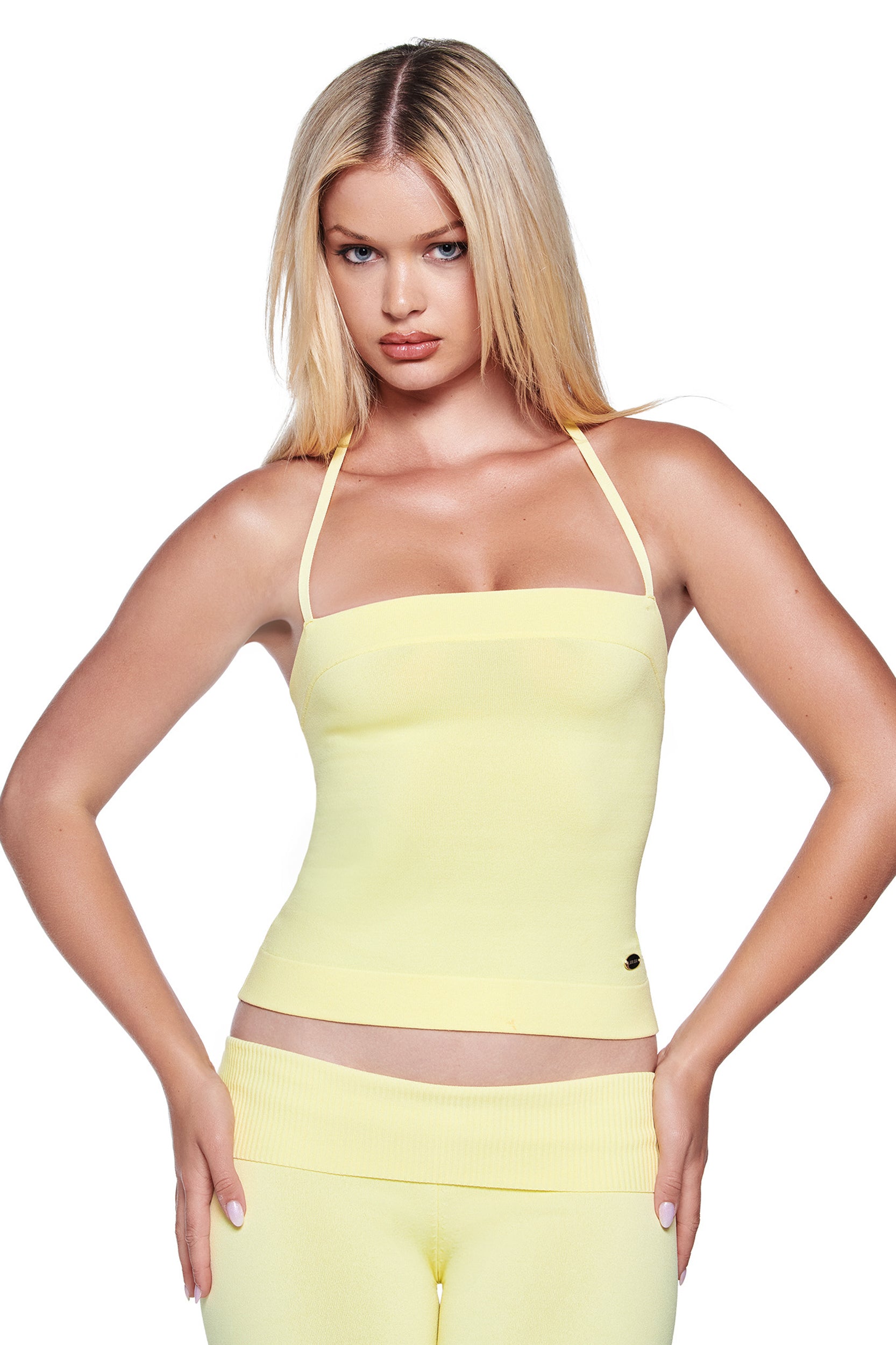 A woman with straight blonde hair wears the I.AM.GIA AUDRINA TOP in baby yellow, paired with matching pants, standing against a white background with her hands on her hips.