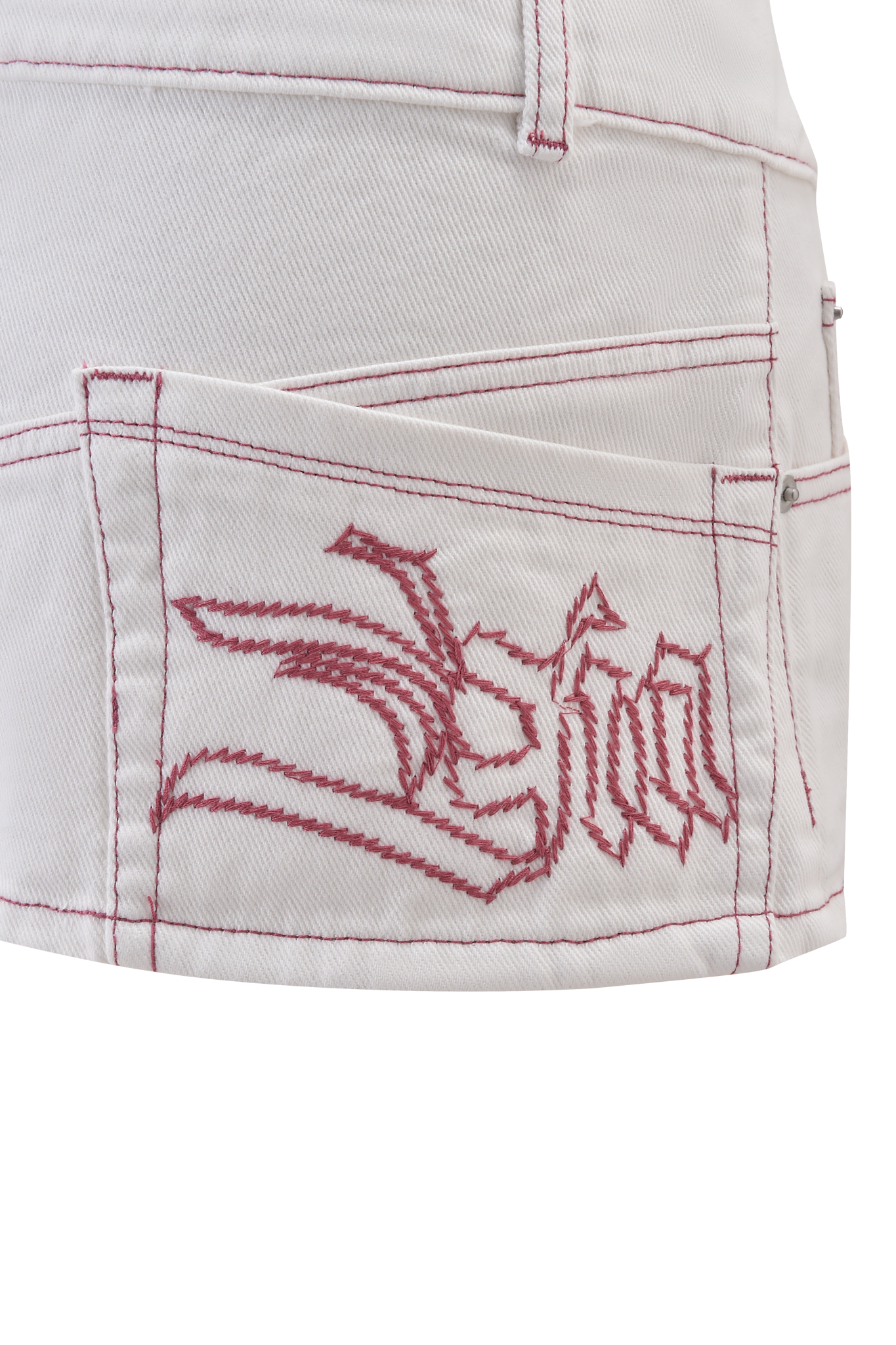 Close-up of the MOXIE DENIM MINI SKORT in white by I.AM.GIA, showing its pocket with hot pink contrast stitching and a decorative embroidered design featuring bold, stylized lines and lettering.