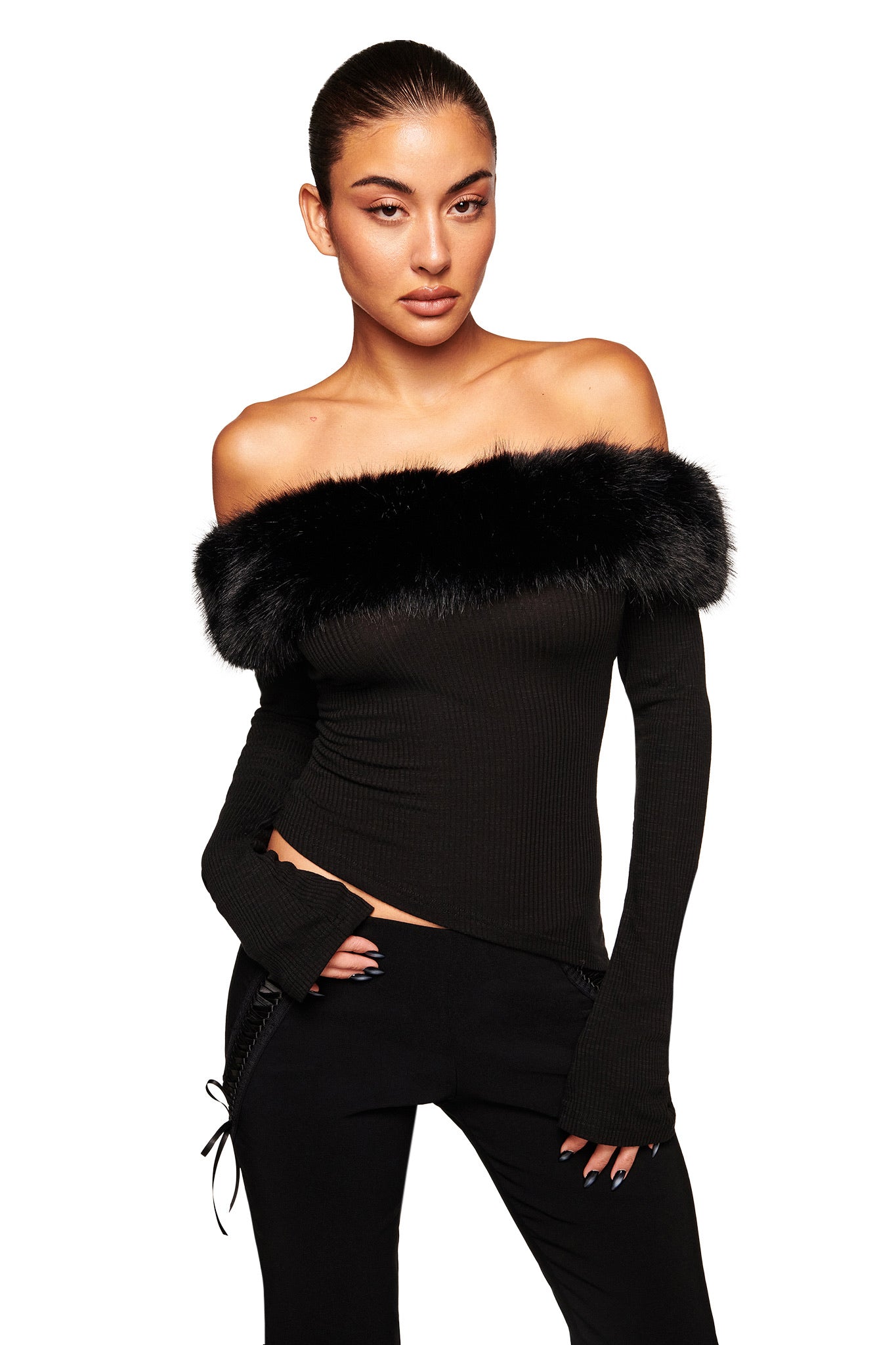A woman wears the I.AM.GIA CECILY TOP in black, featuring an off-shoulder design with a faux fur collar, paired with black pants. Her hair is styled back as she poses against a plain white background.