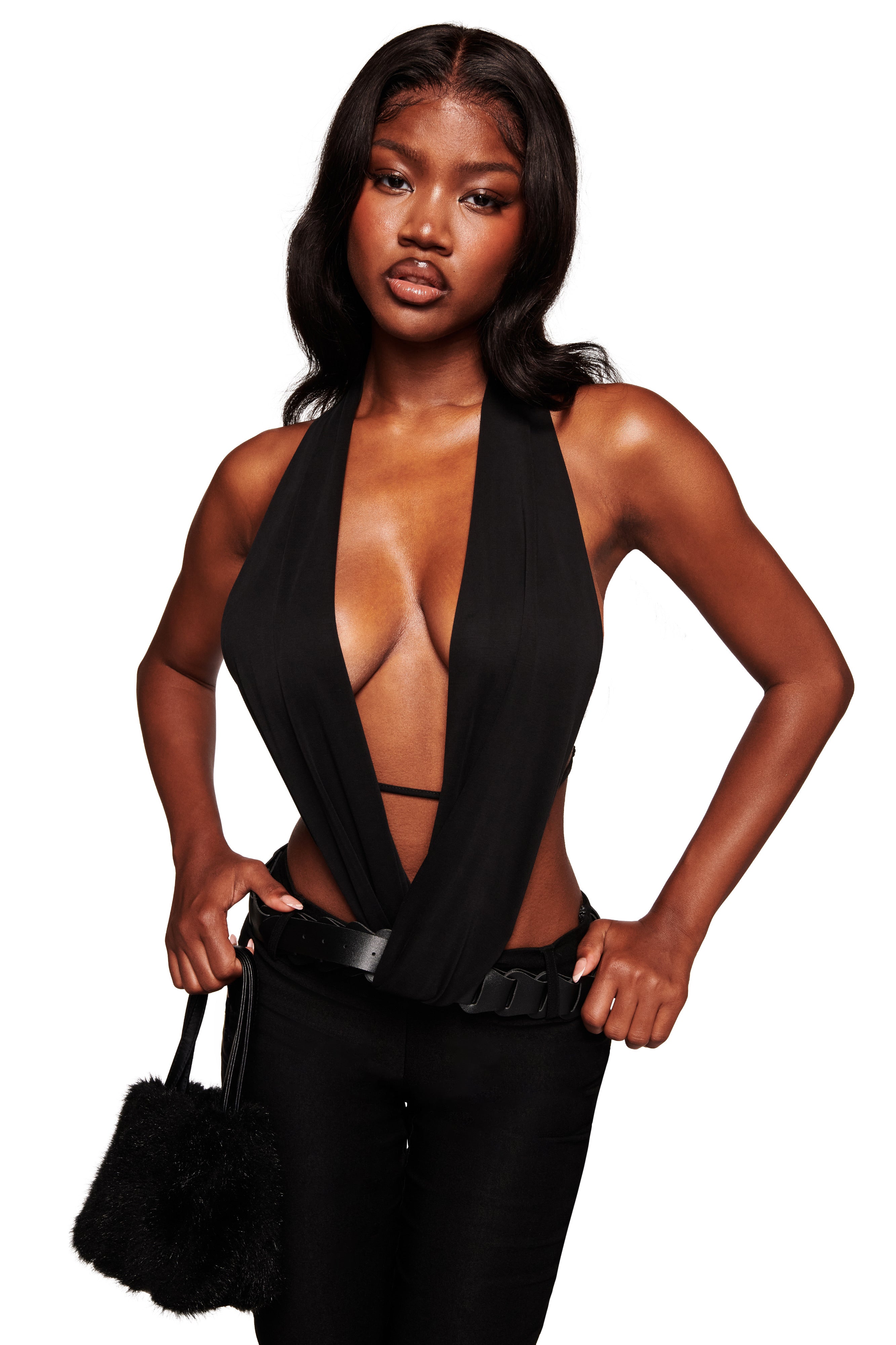 A woman with long, dark hair wears the I.AM.GIA SALDANA TOP in black and matching black pants, holding a small black furry handbag with an adjustable strap. She stands confidently against a white background.